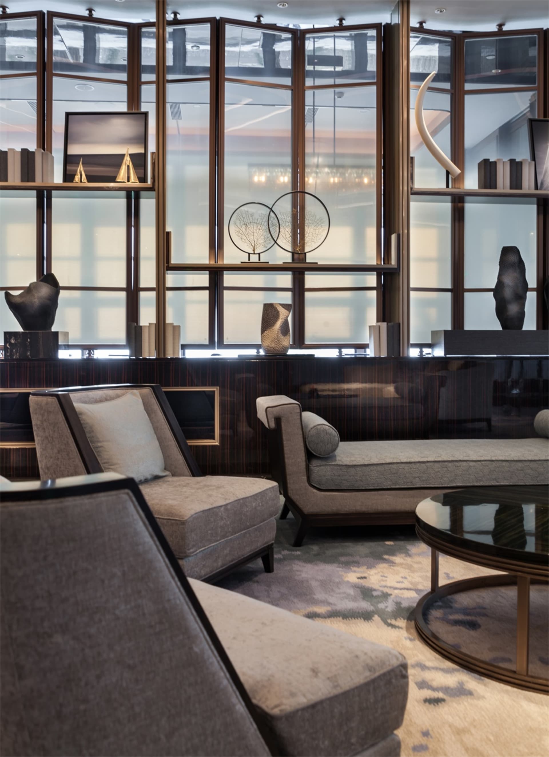 A modern living room with neutral-toned sofas and a coffee table, featuring decorative elements on shelves and a large window