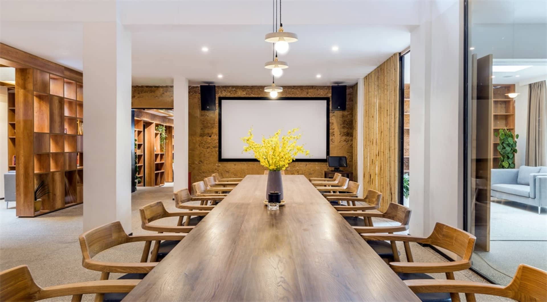 A modern office conference room with a wooden table, chairs, and a projector screen.
