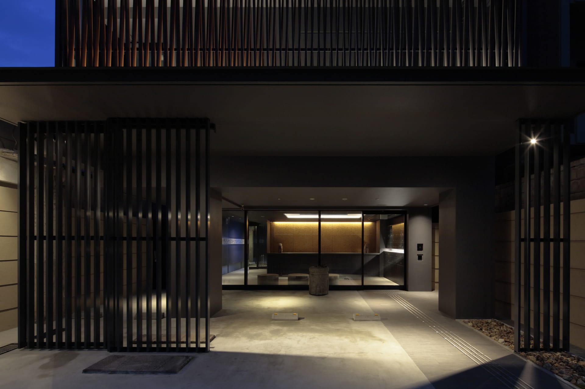 A modern, geometric entrance featuring metal gates and concrete flooring at dusk.