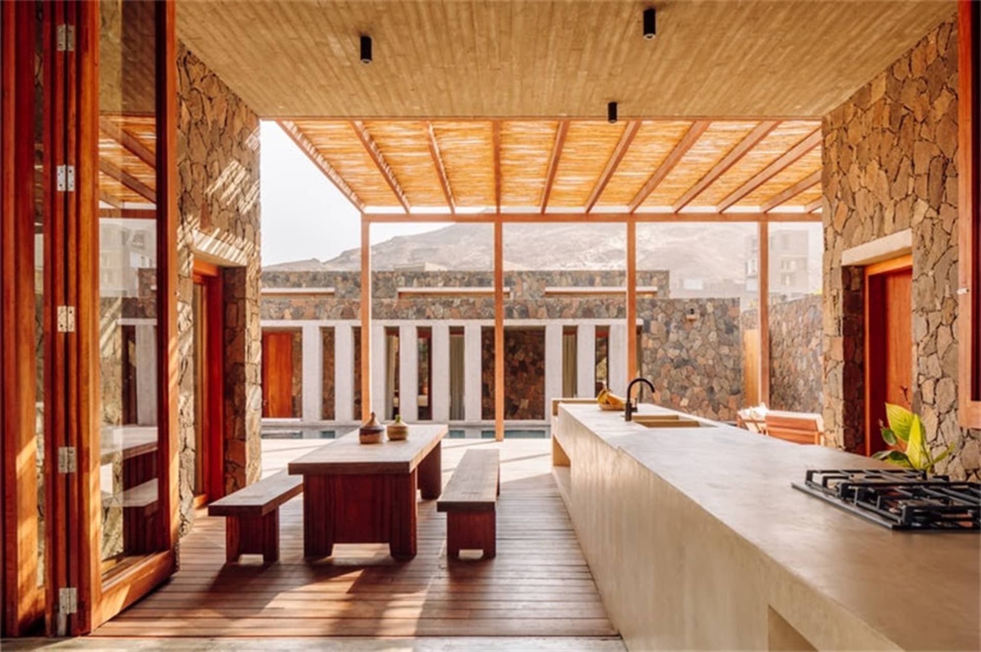 An industrial-style residential kitchen featuring concrete countertops and walls with a natural stone patio and outdoor seati