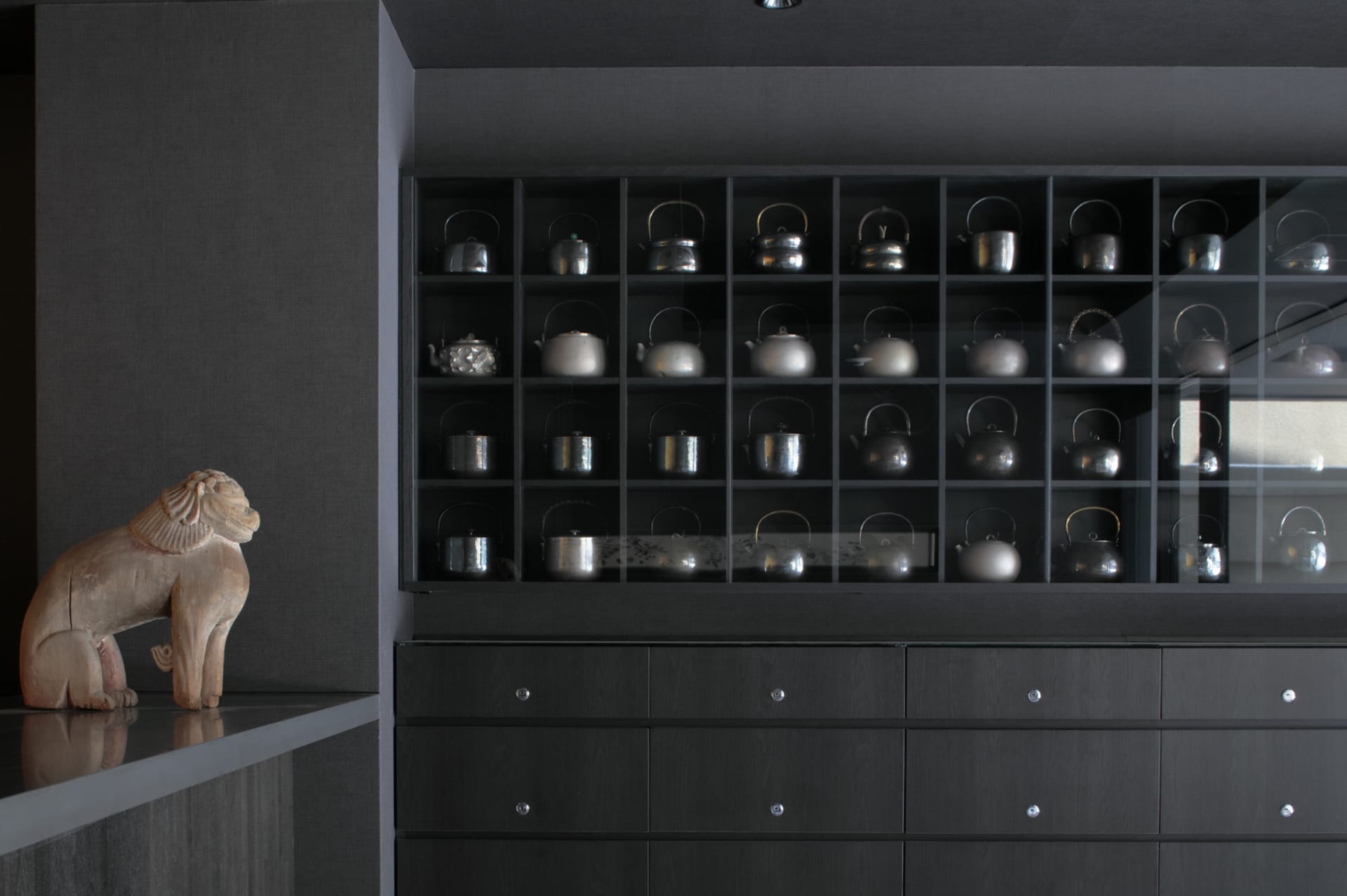 Various metallic teapots organized in black cabinetry in a tea room setting.