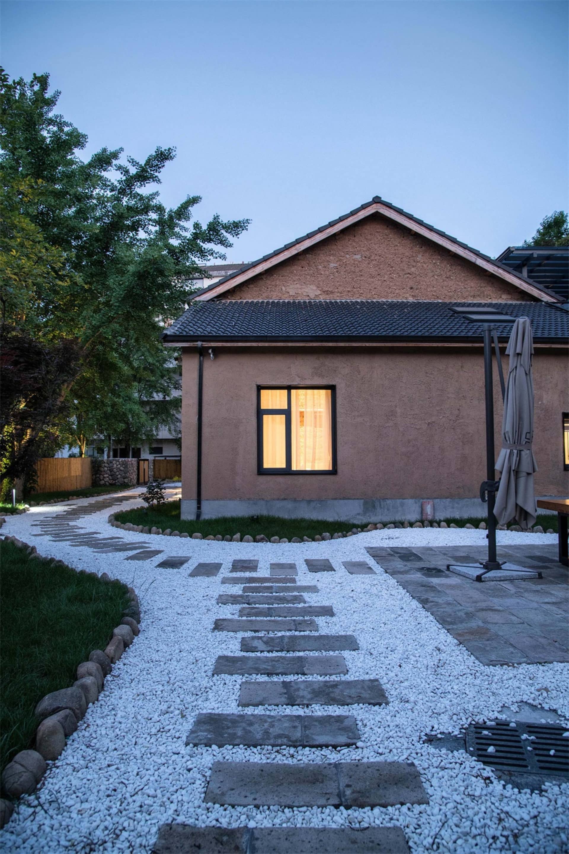 一座擁有混凝土外牆的現代房屋，設有步道與黃昏時分點亮的窗戶。