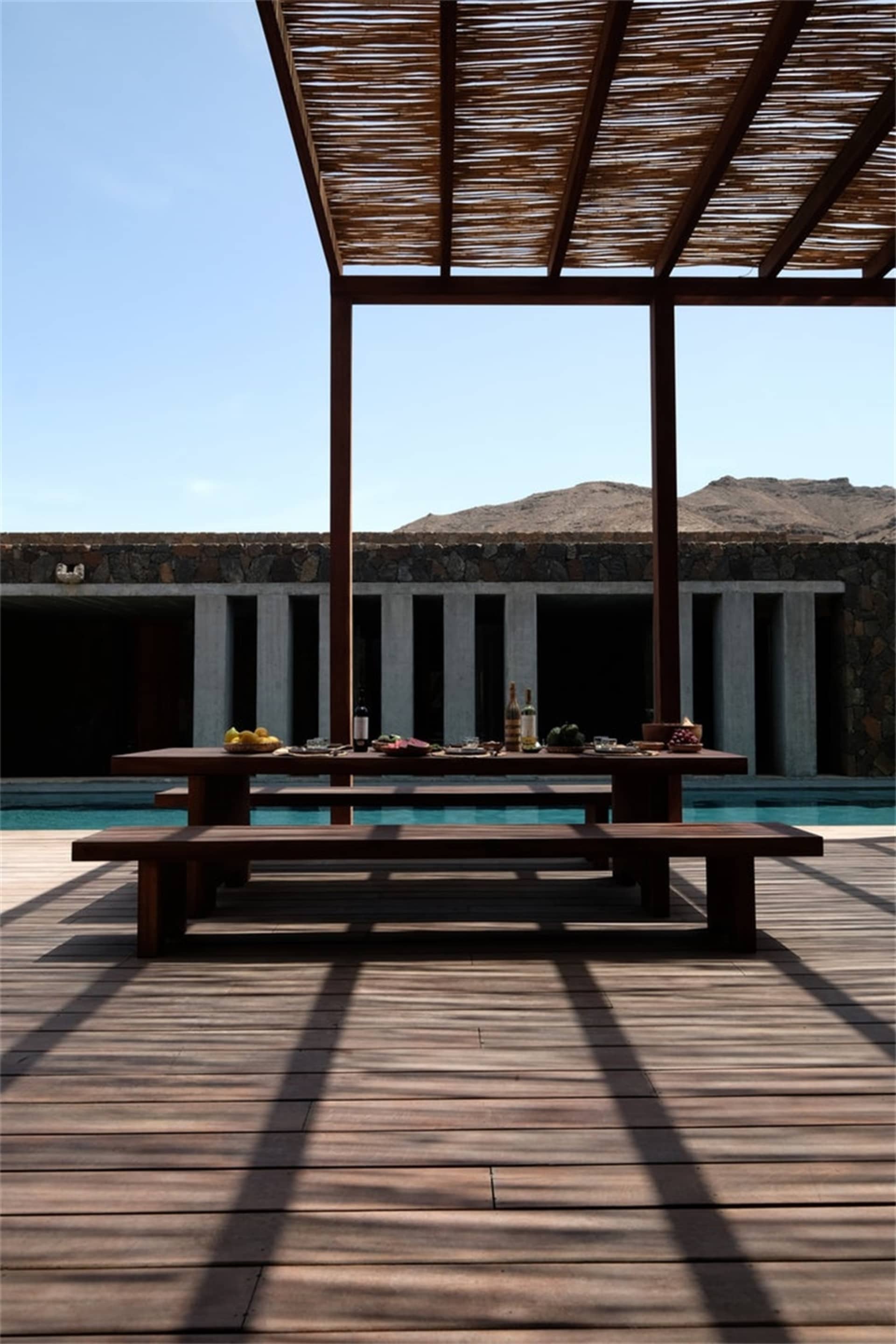 Outdoor wooden dining area with a table set for a meal, featuring a pergola and a scenic mountain backdrop.