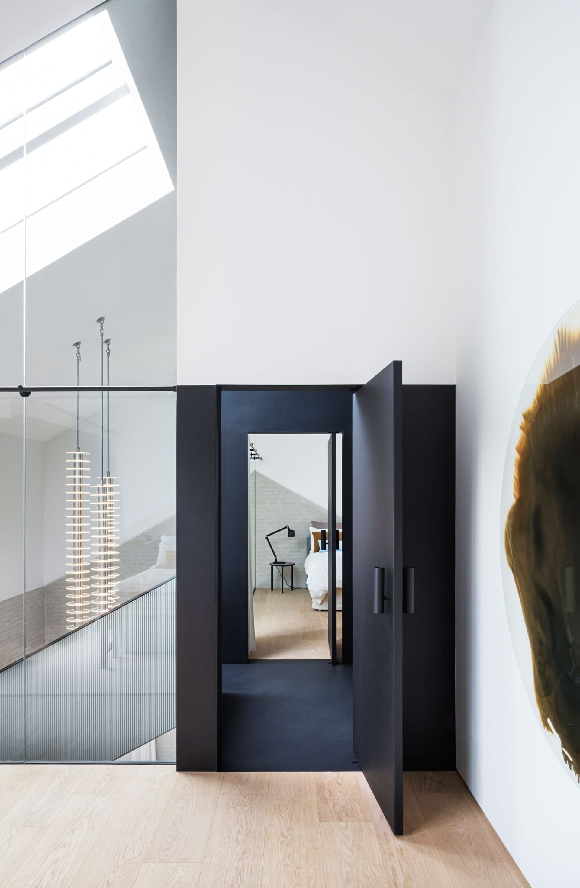 A modern bedroom featuring a black glass door and a large glass window, with a minimalist interior design.