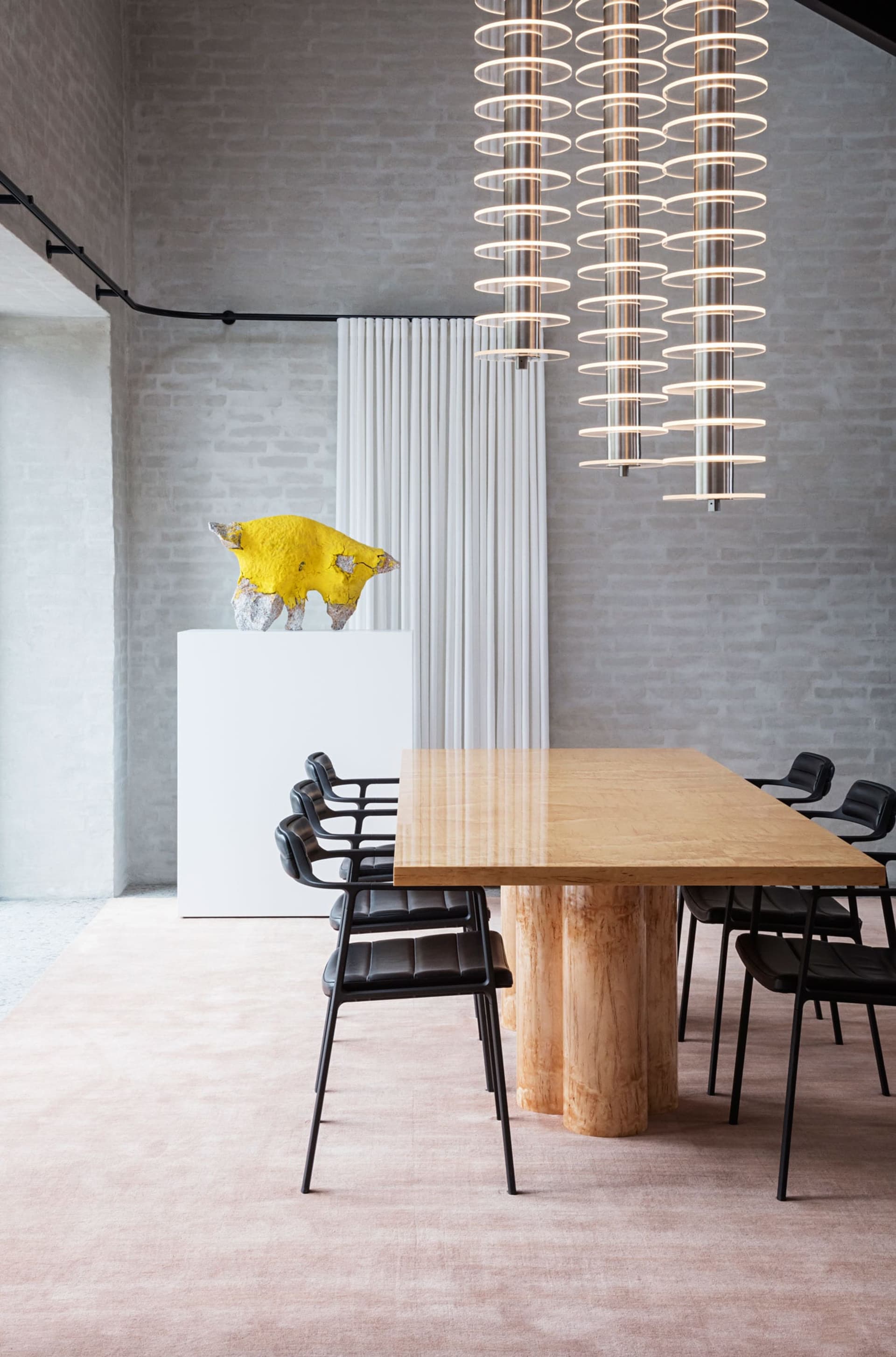 A modern dining room with timber table, black chairs, and a yellow art sculpture on a white pedestal.