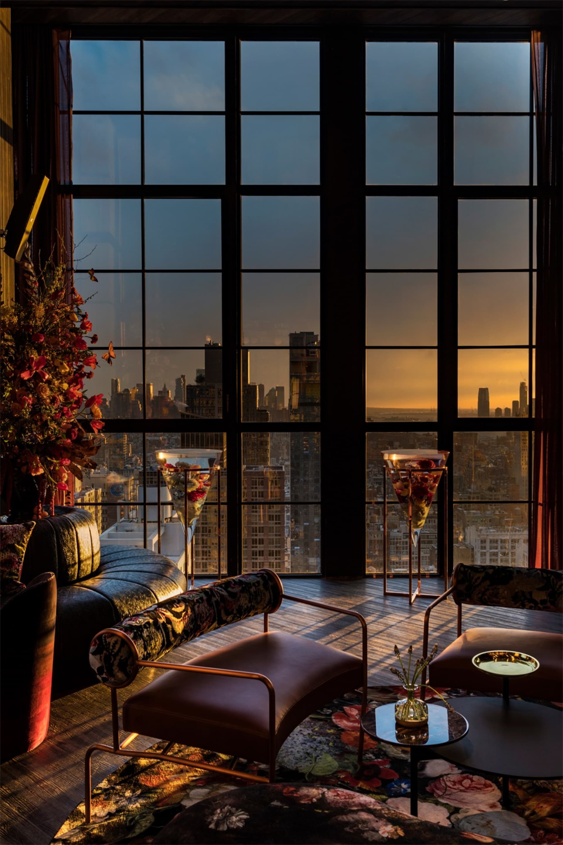 Modern living room with a glass window overlooking a cityscape during sunset.