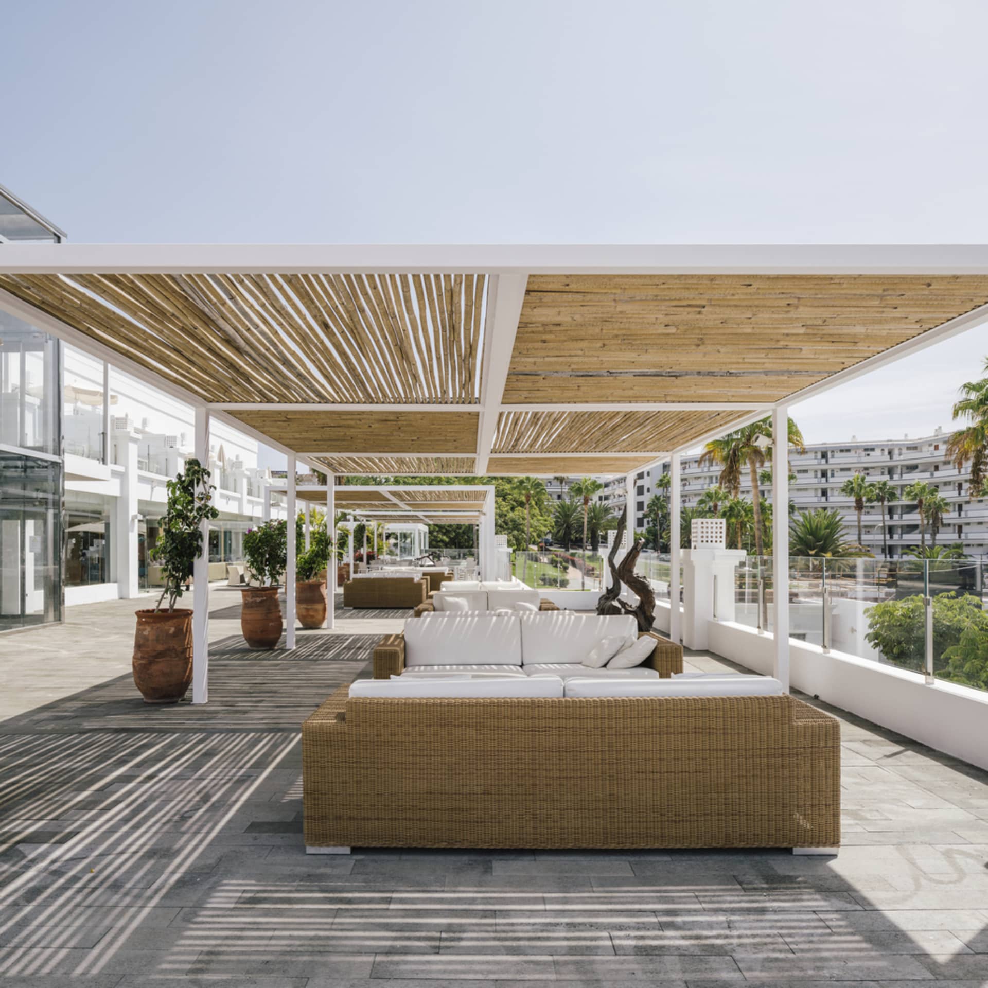 Outdoor lounge area with wicker furniture and white cushions under a wooden pergola.