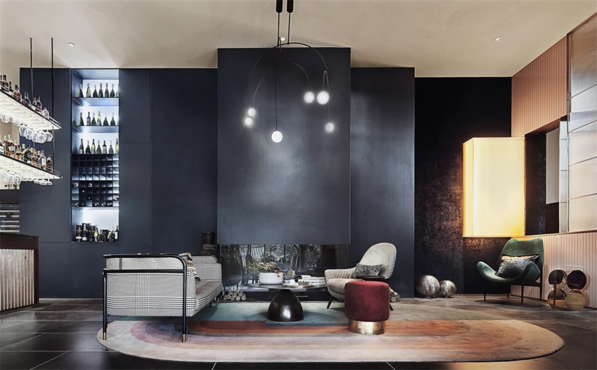 A modern bar lounge with metal, glass, and leather materials, featuring a circular rug, seating, and a bar area.