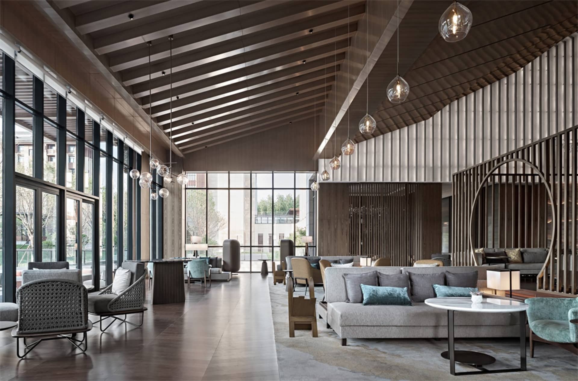 A spacious, modern industrial hotel lobby featuring glass walls, concrete flooring, and wooden accents.