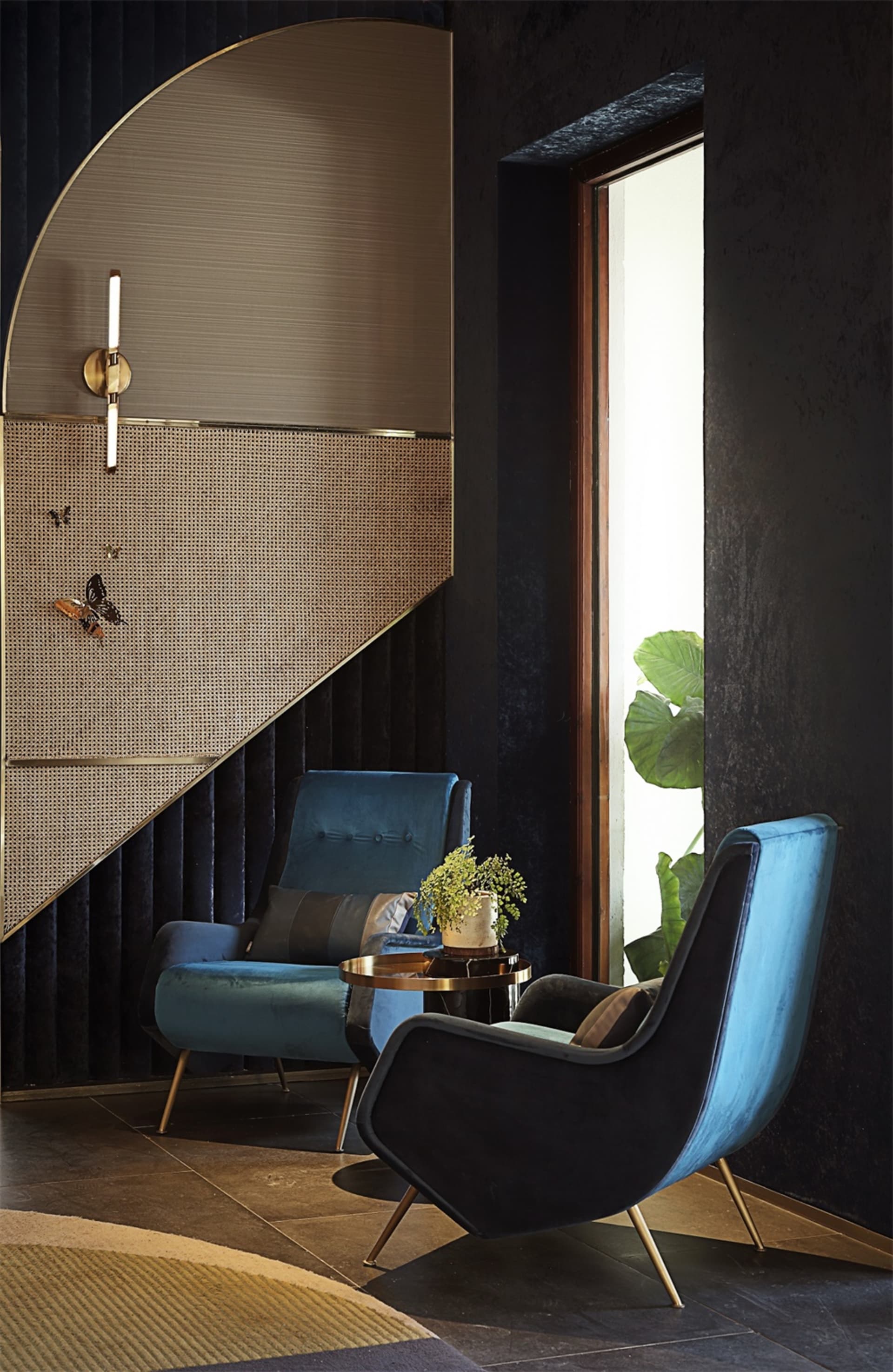 Modern lobby with two blue upholstered armchairs and a small round side table with a plant on it, positioned near a large win