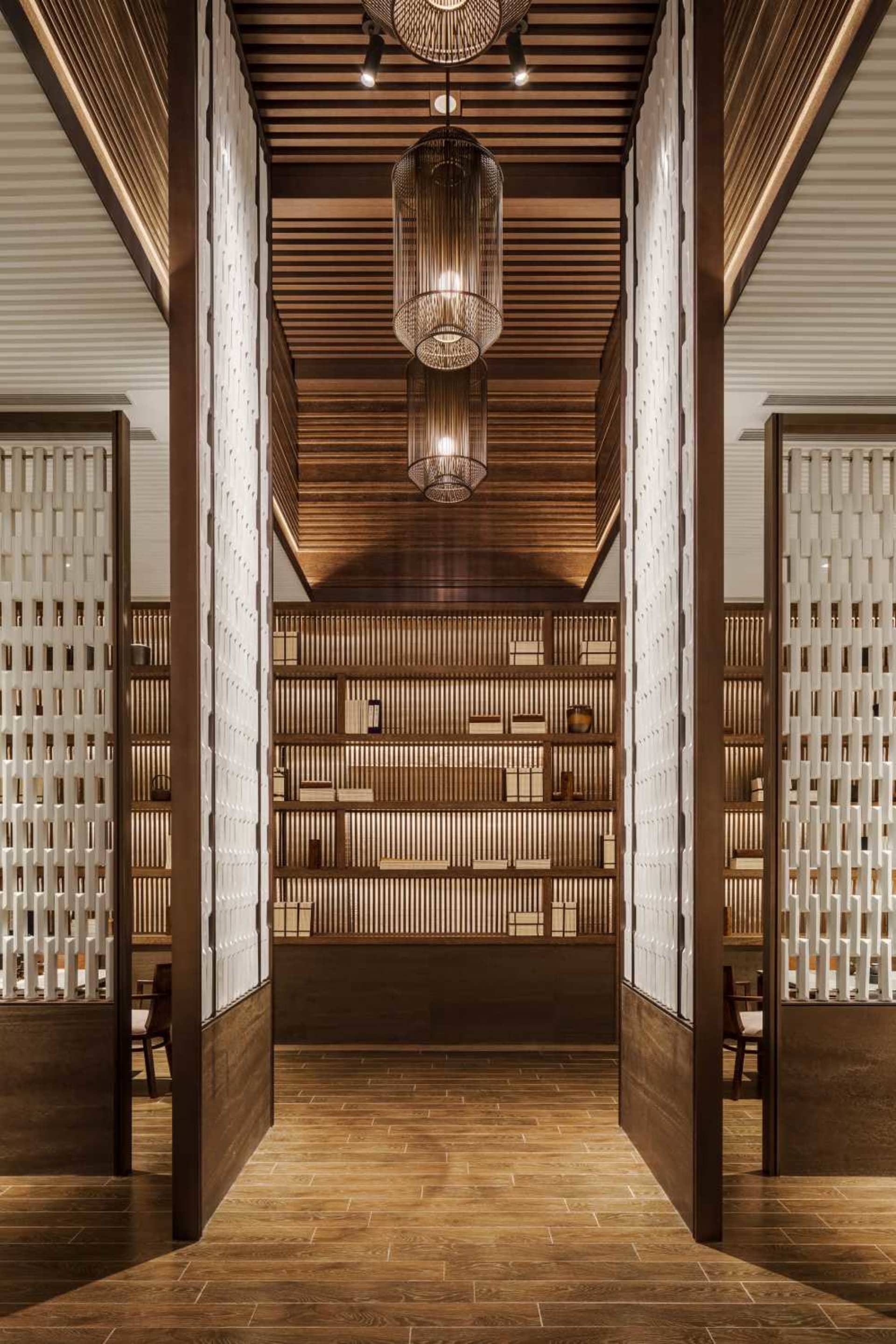 A modern wooden library with shelves filled with books and wooden light fixtures hanging from the ceiling.