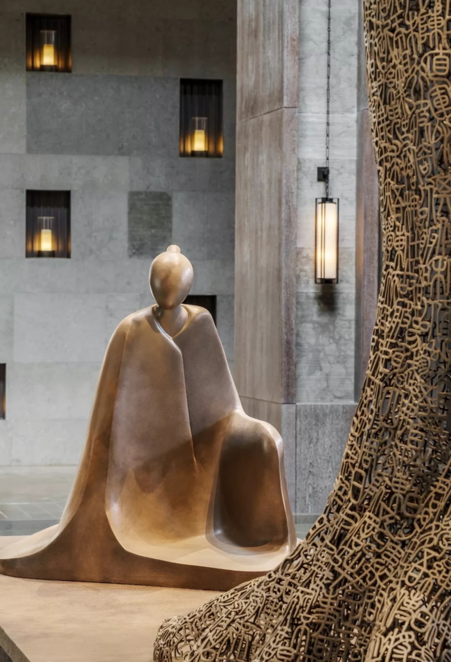 A metal statue of a seated figure in a lobby setting.
