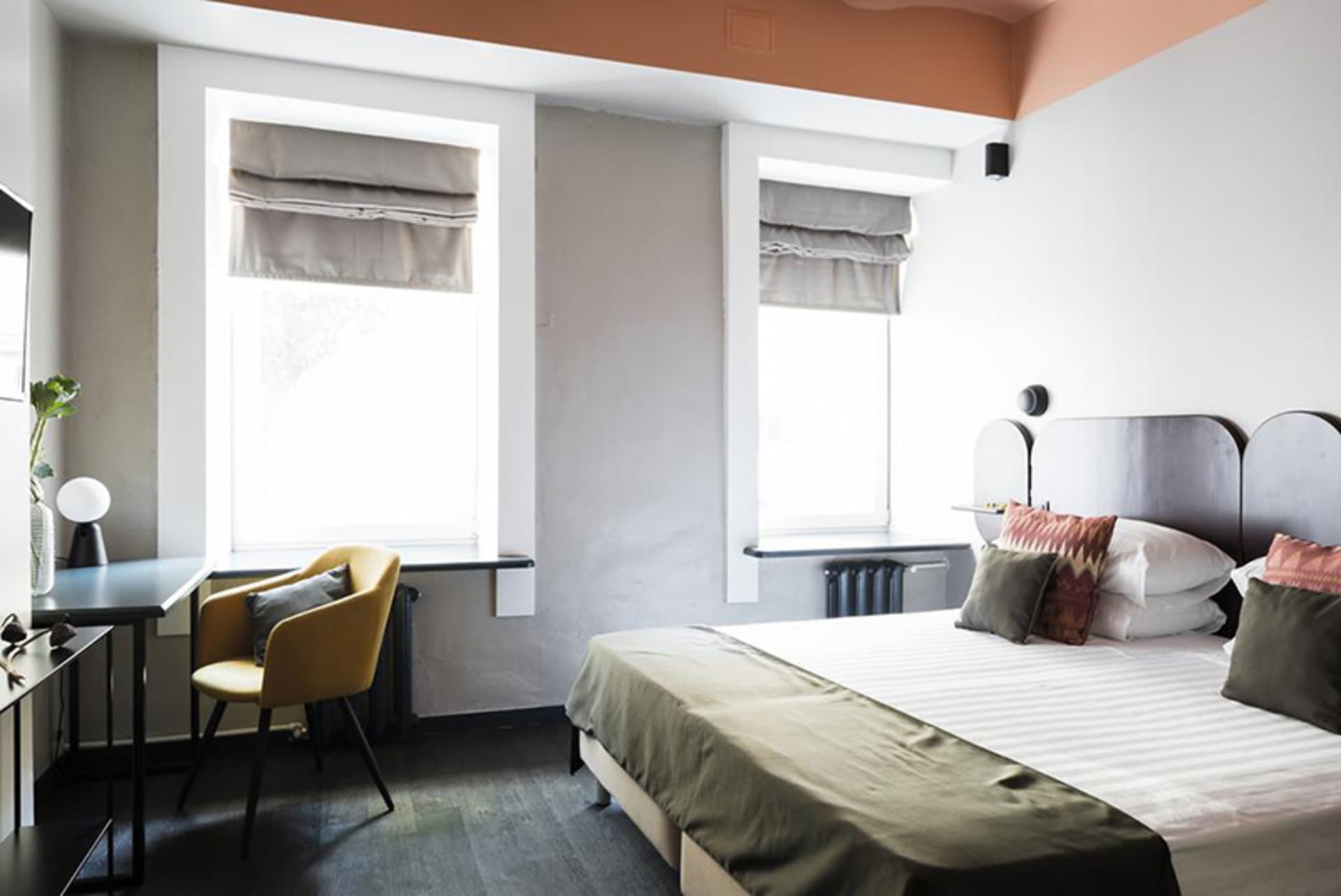 A minimalist bedroom with a white bed, green blanket, and simple decor.