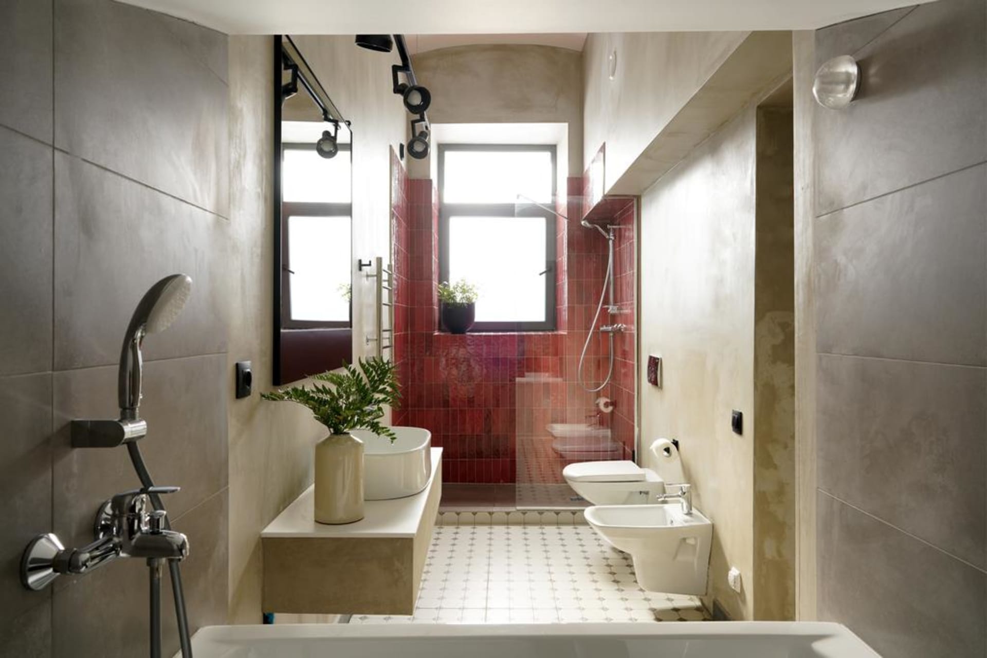 A modern bathroom featuring red and white ceramic tiles with a white freestanding bathtub, a white toilet, a white bidet, and