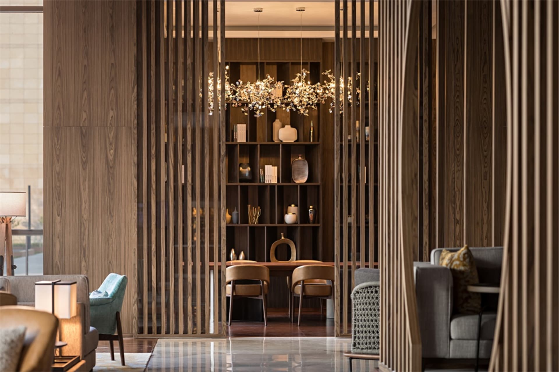 A modern living room with wooden walls, floor, and furniture, featuring a bookshelf with decorative items and a chandelier wi