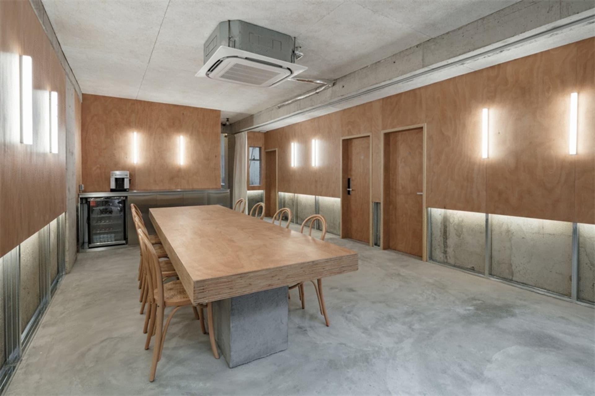 An industrial conference room with a wooden table, chairs, and concrete walls and floor.