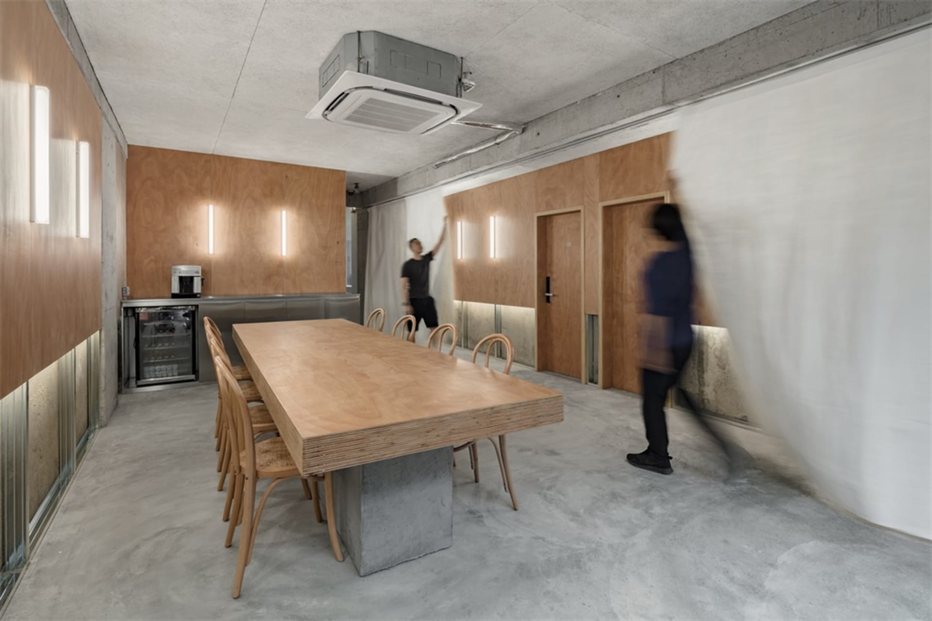 A spacious, industrial-style office with concrete floors, plywood walls, and steel fixtures, featuring a large wooden table a