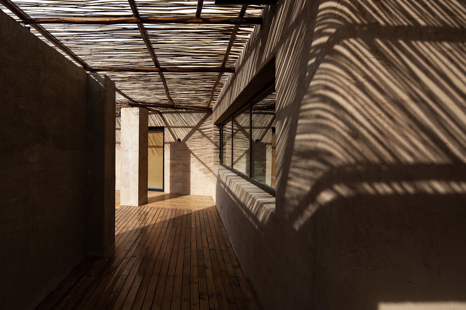 A modern rooftop terrace with natural lighting, featuring wooden flooring and a woven bamboo roof structure, providing a comf