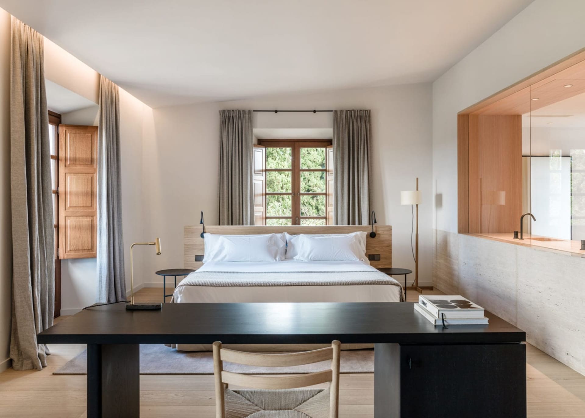 A modern minimalist bedroom with a large bed, white furniture, and wooden floors.