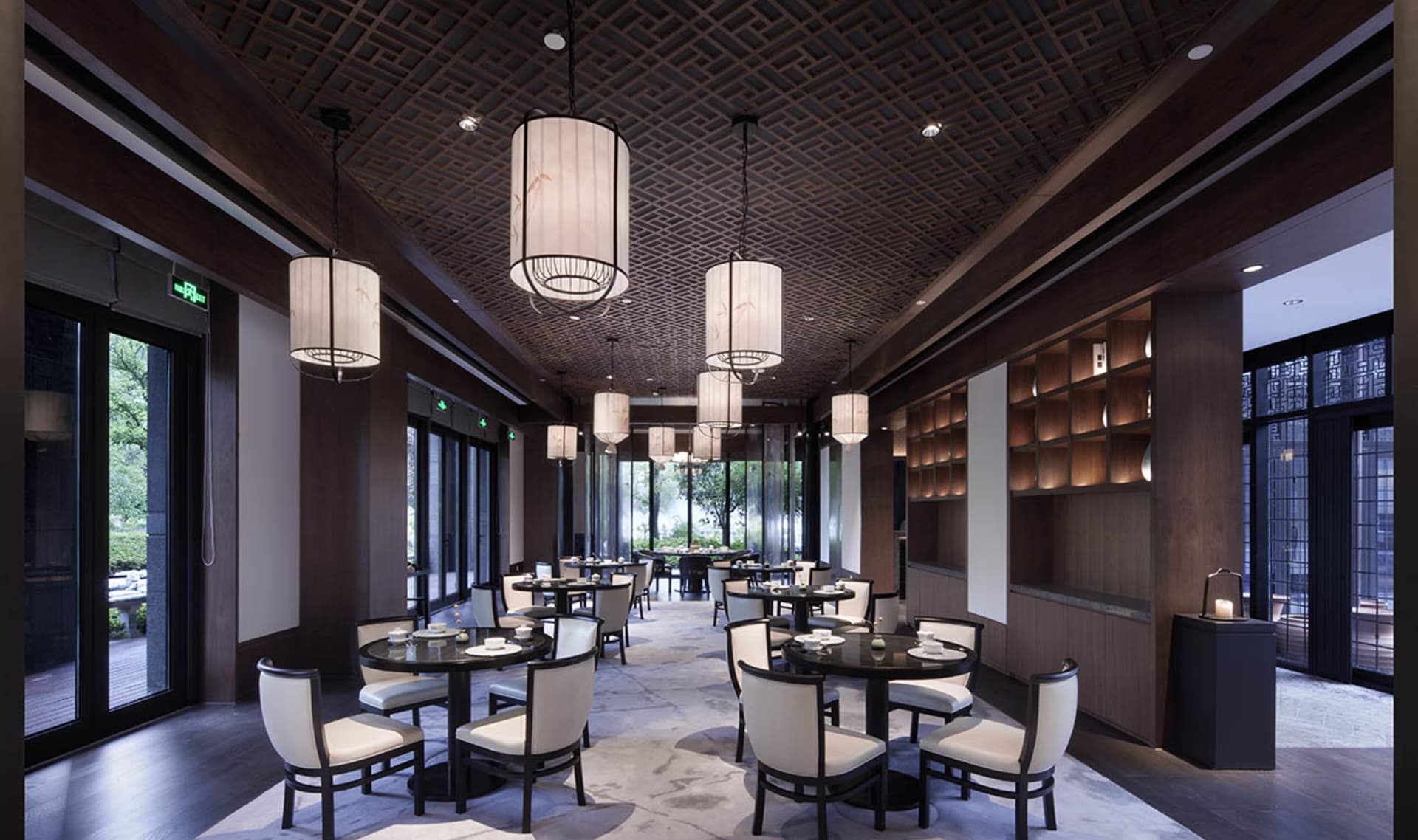 現代餐廳室內,配有圓形餐桌、白椅、大型窗戶與裝飾天花板。