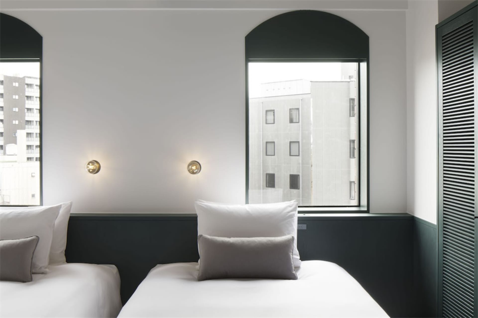 A minimalist hotel room with white walls and bedding.