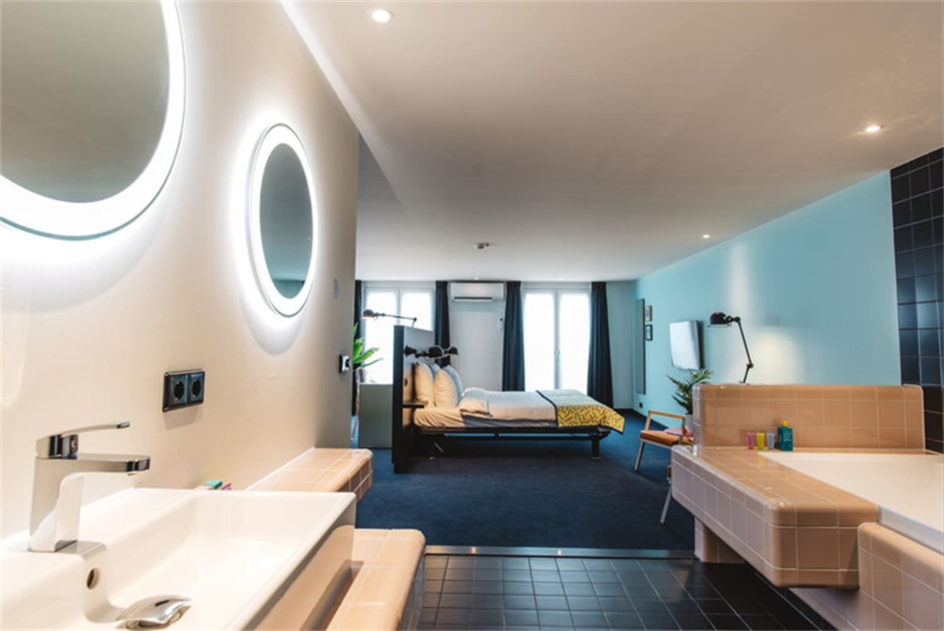 Contemporary hotel room featuring modern furnishings, tiled flooring, concrete accents, and a spacious layout with a bed, sin