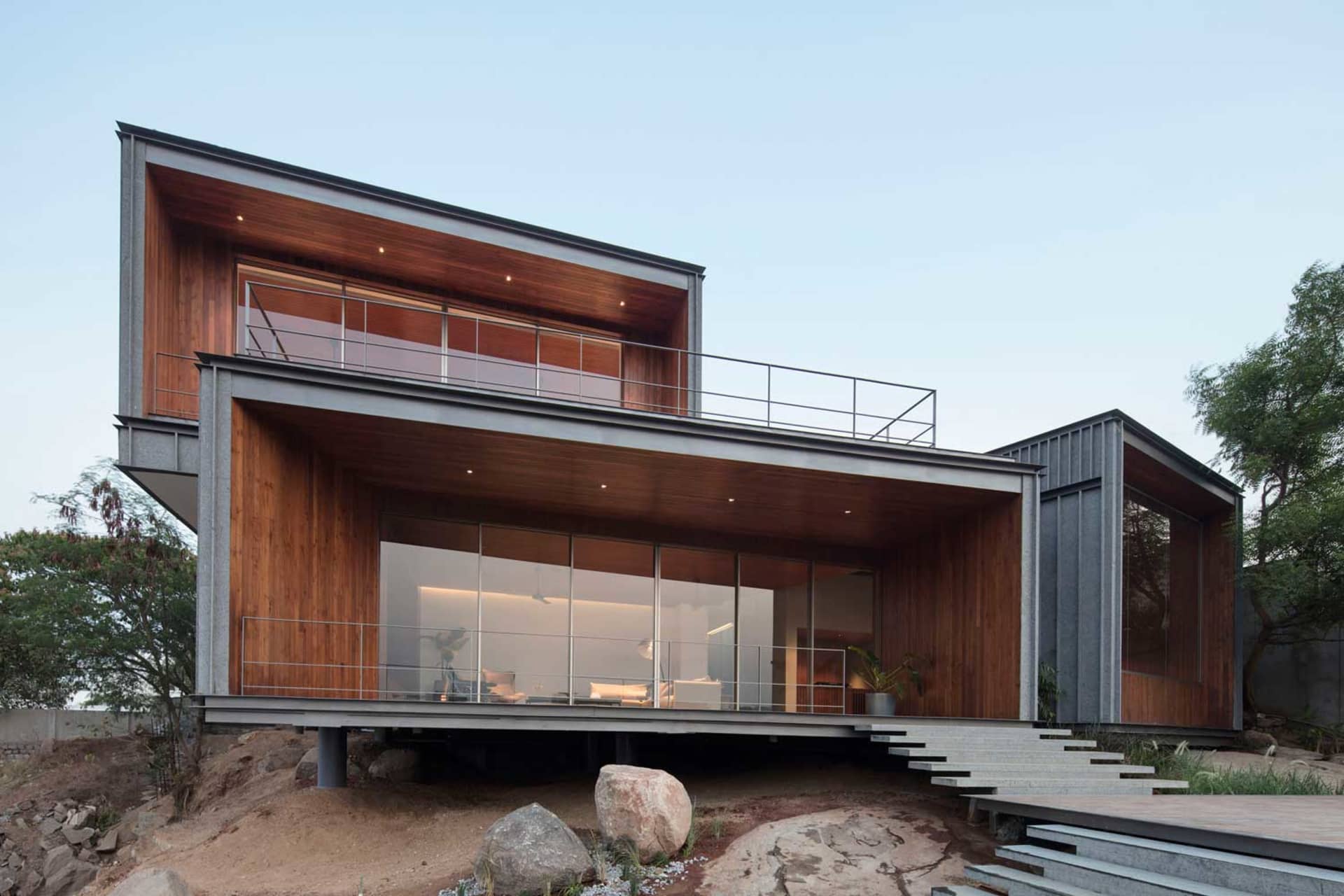 A modern, two-story house with industrial design features, including wood siding, large glass windows, and concrete steps.