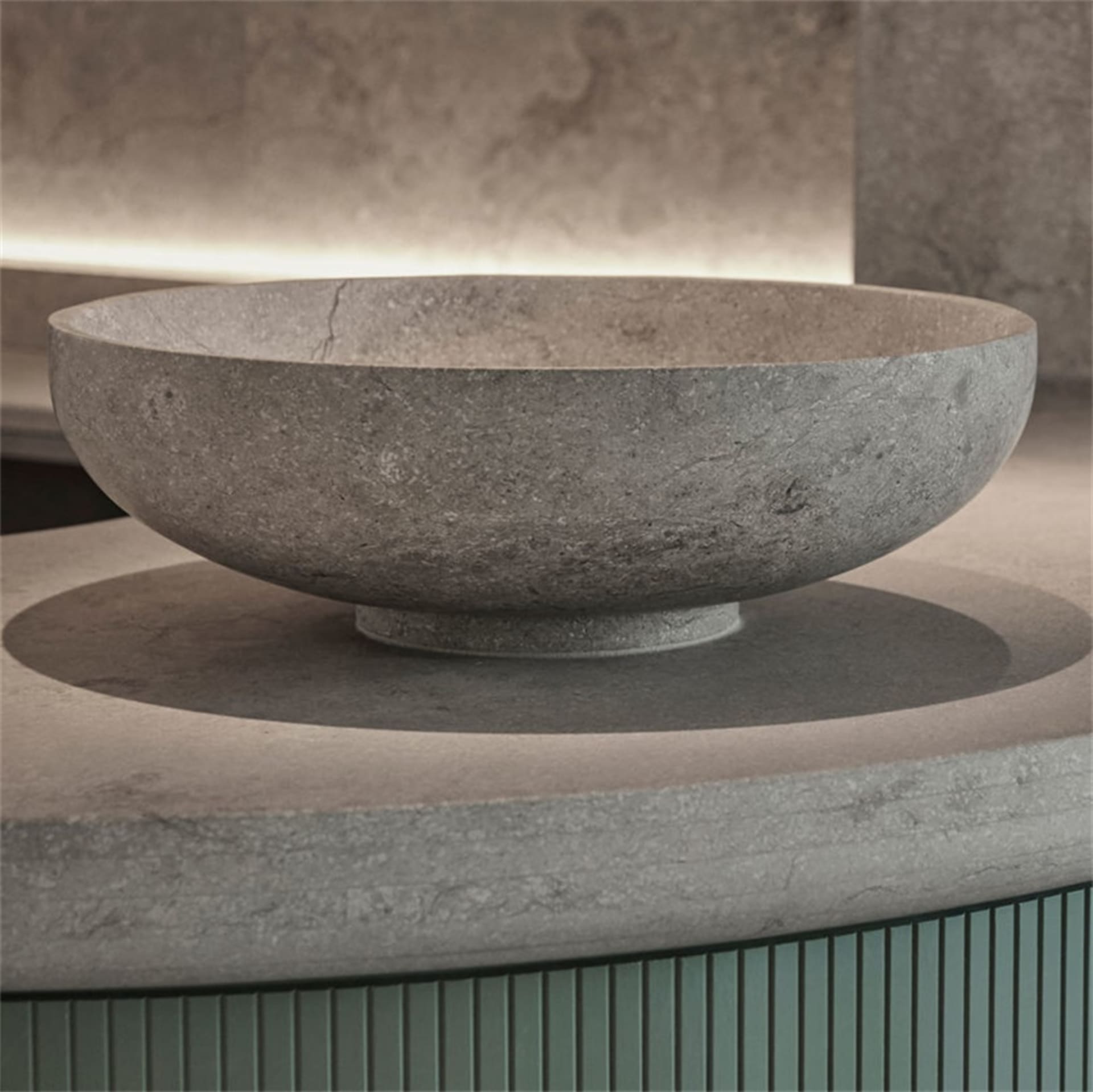 A minimalist, circular concrete bowl with a textured surface placed on a concrete surface.