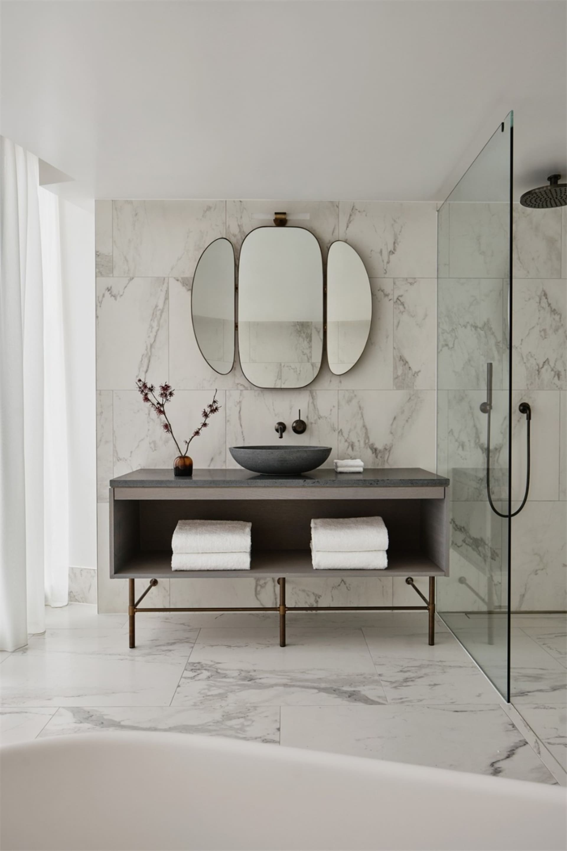 A modern bathroom with marble tile walls and floor, featuring a floating vanity, a black stone sink, and a walk-in shower wit