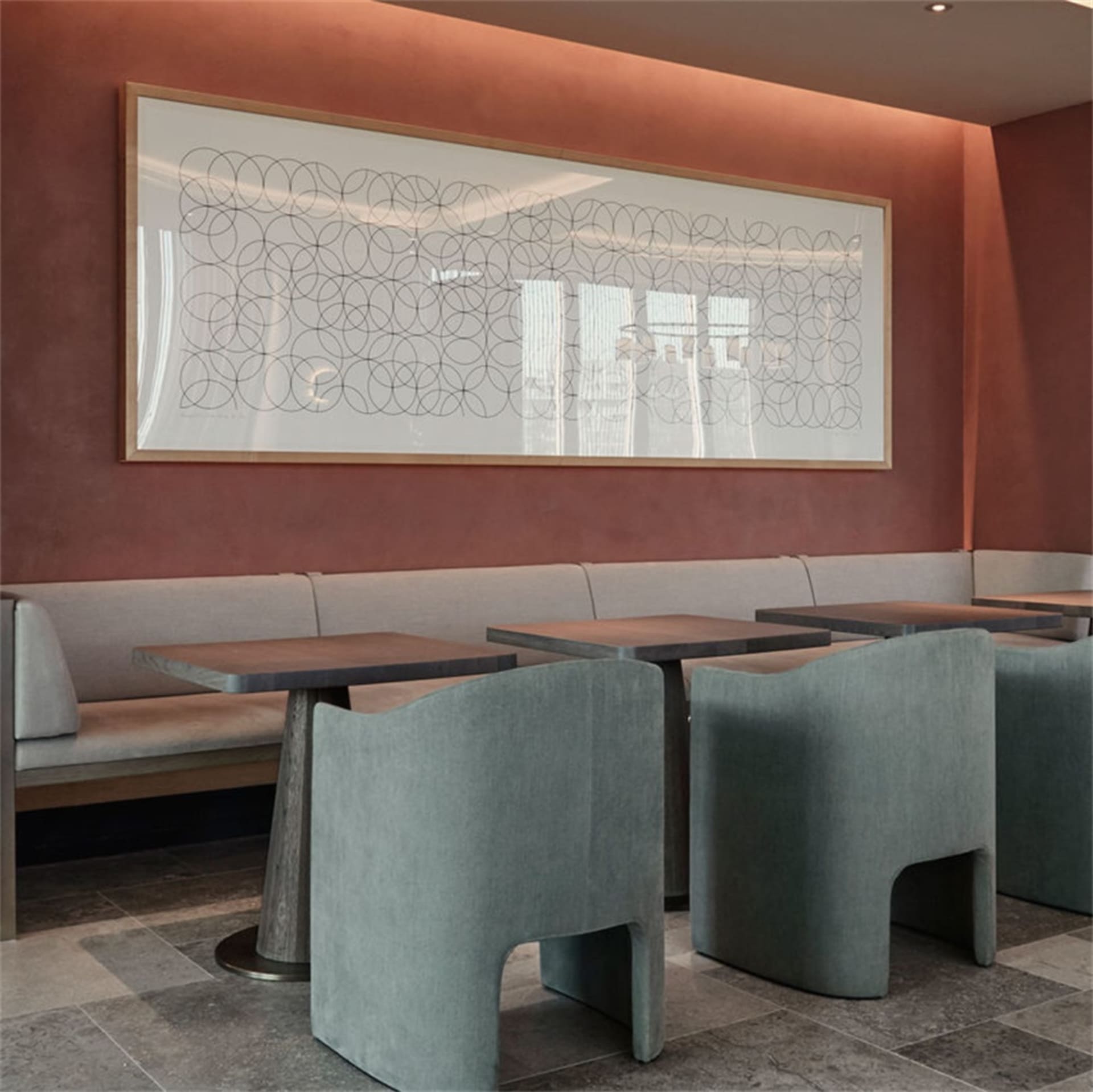 A modern restaurant interior featuring concrete furniture and a geometric wall art piece.