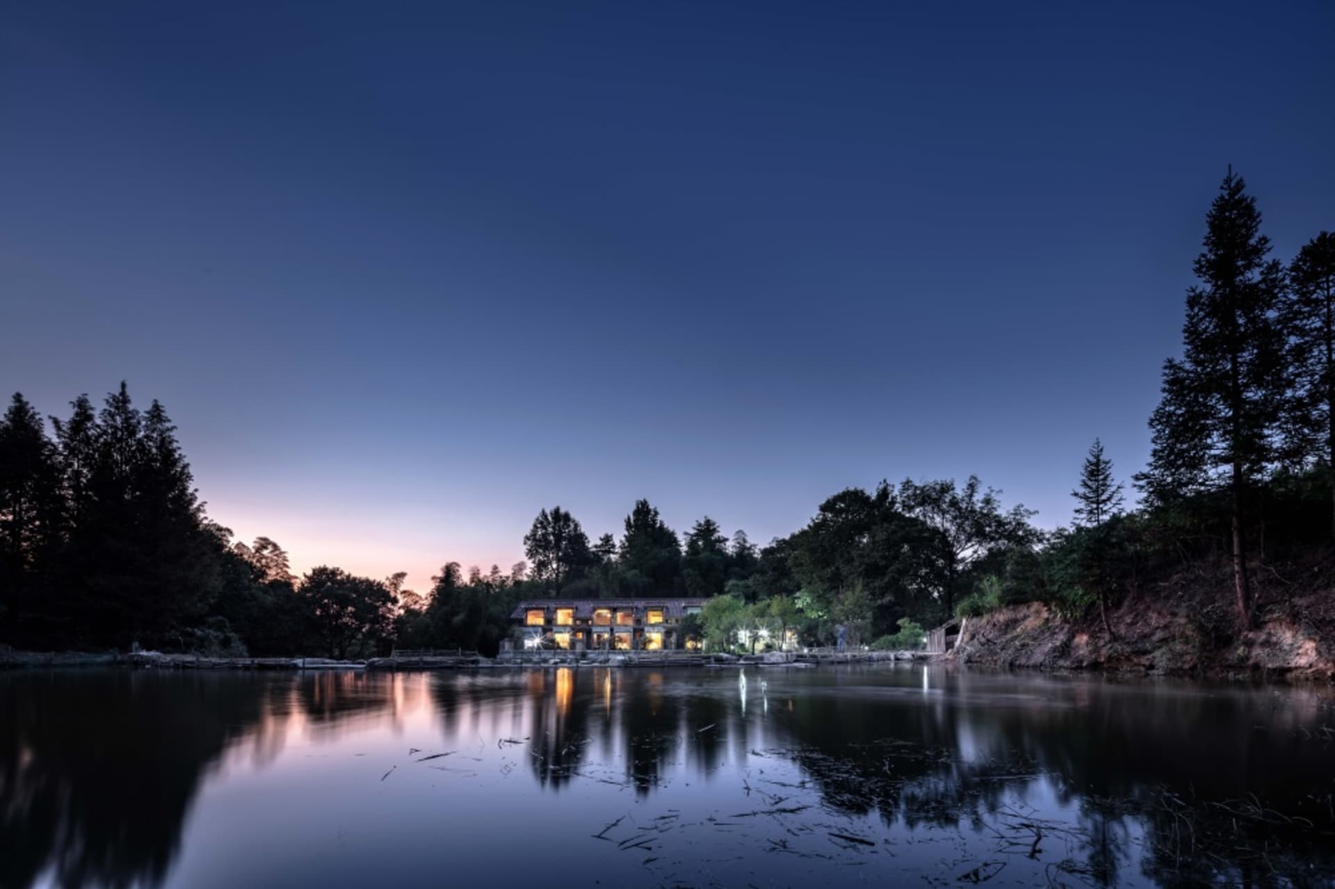 A cozy residential lodge made of natural wood surrounded by trees and a serene lake during twilight.
