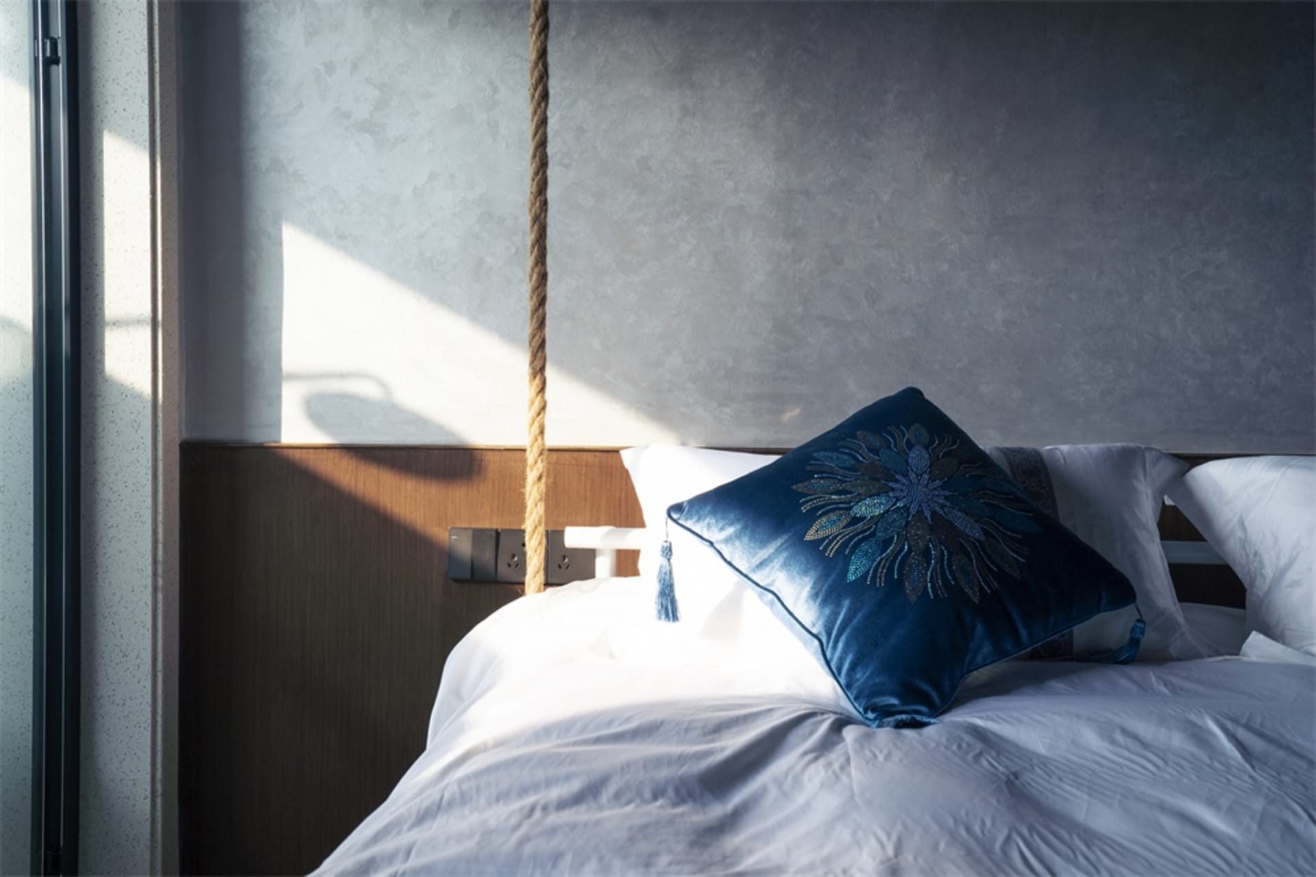 A modern bedroom with white cotton bedding, a blue decorative pillow, and a wooden headboard.