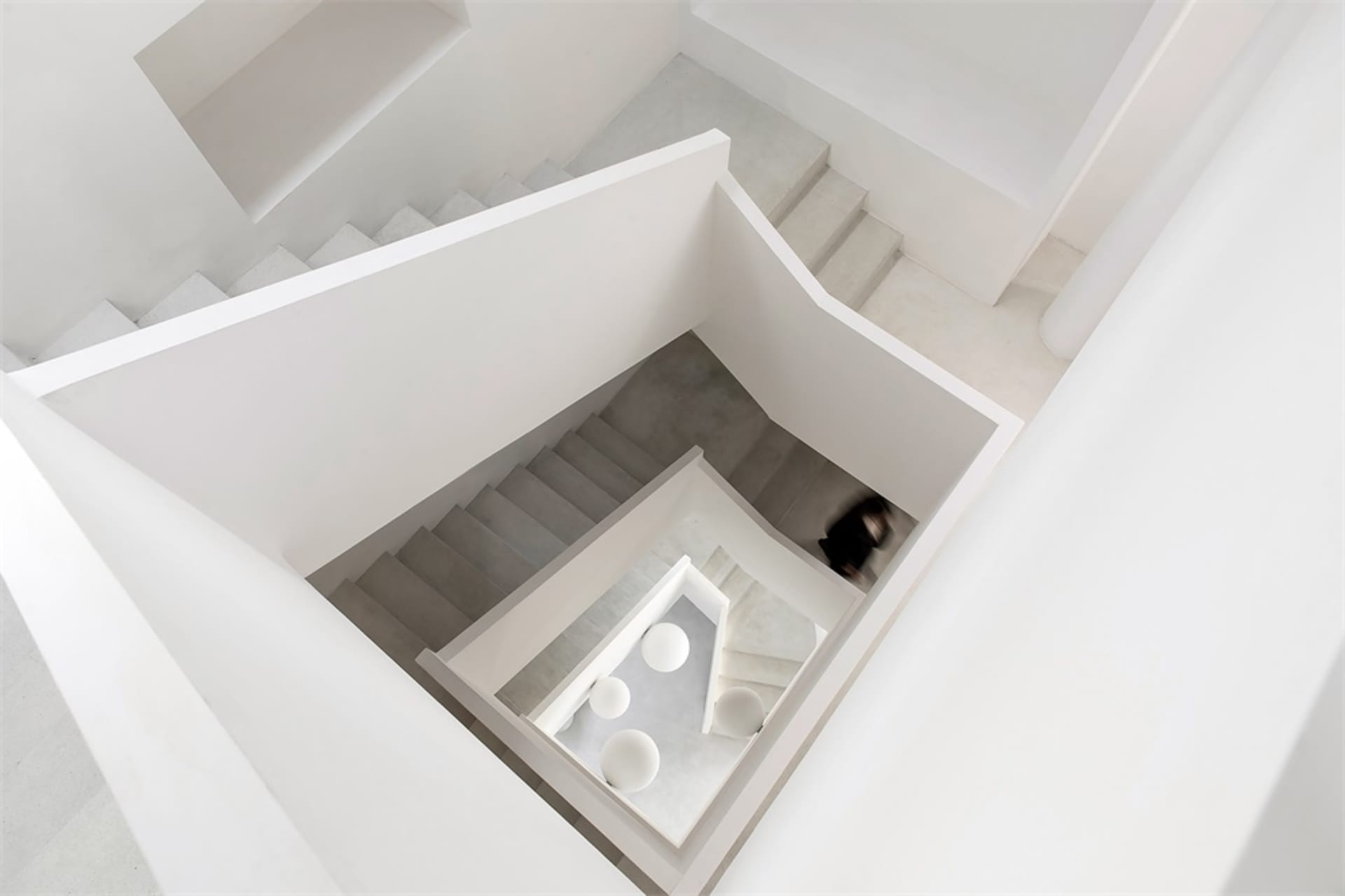 A modern interior with concrete flooring, viewed from above with a person walking on a different level.