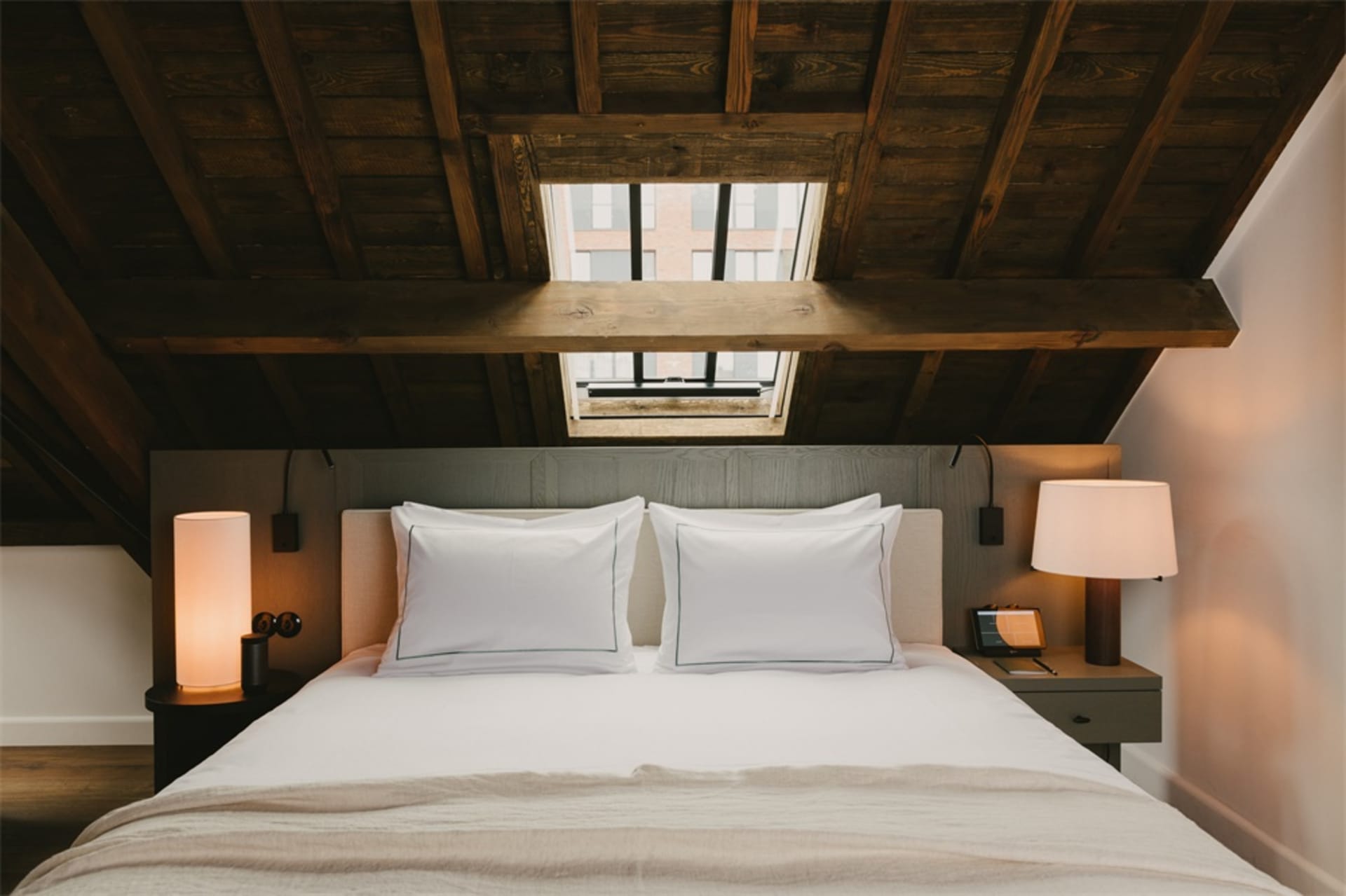 A modern minimalist bedroom with a double bed, white linens, and a skylight in the ceiling.
