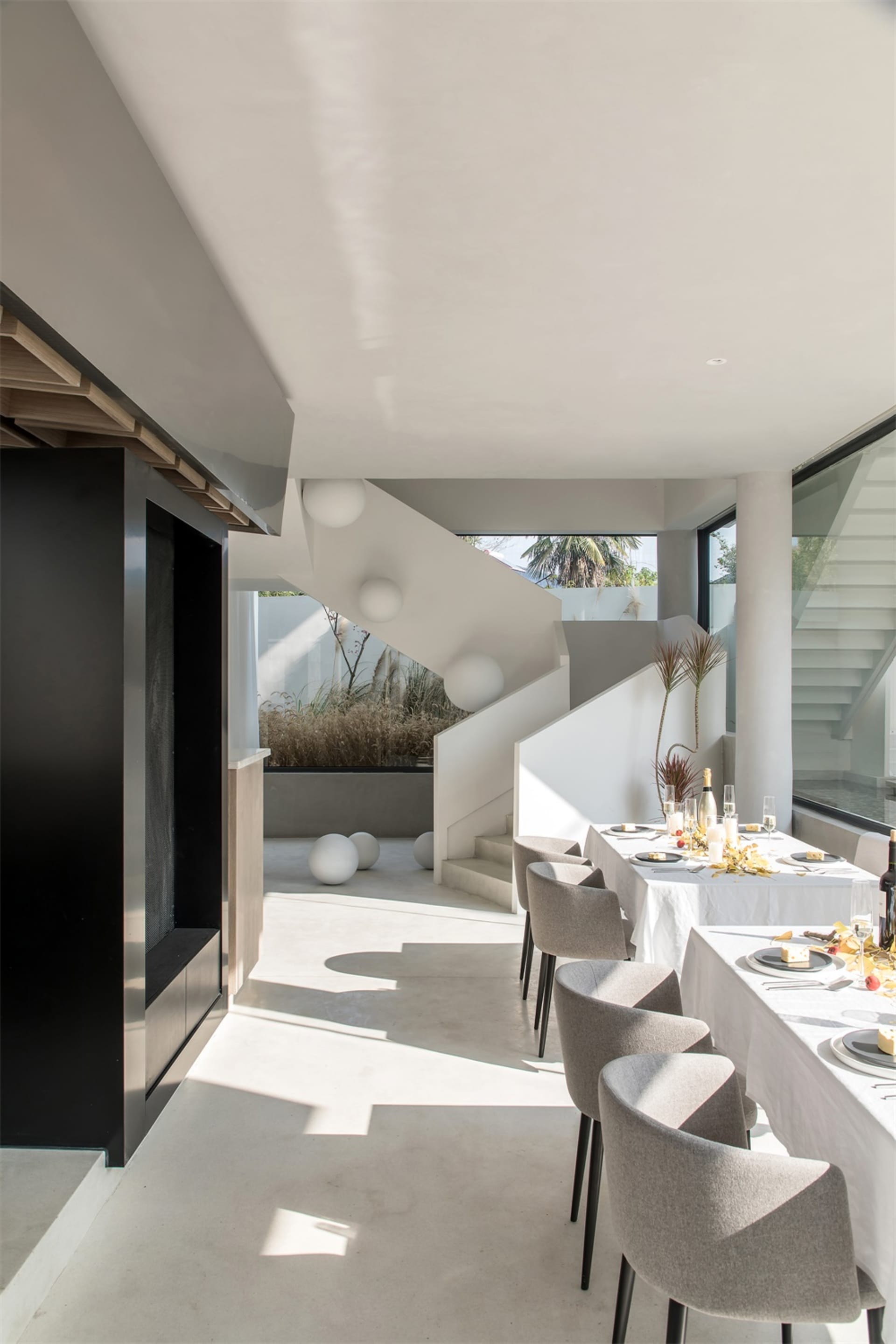 Modern residential dining area with concrete floor, glass walls, and white dining table set for a meal.