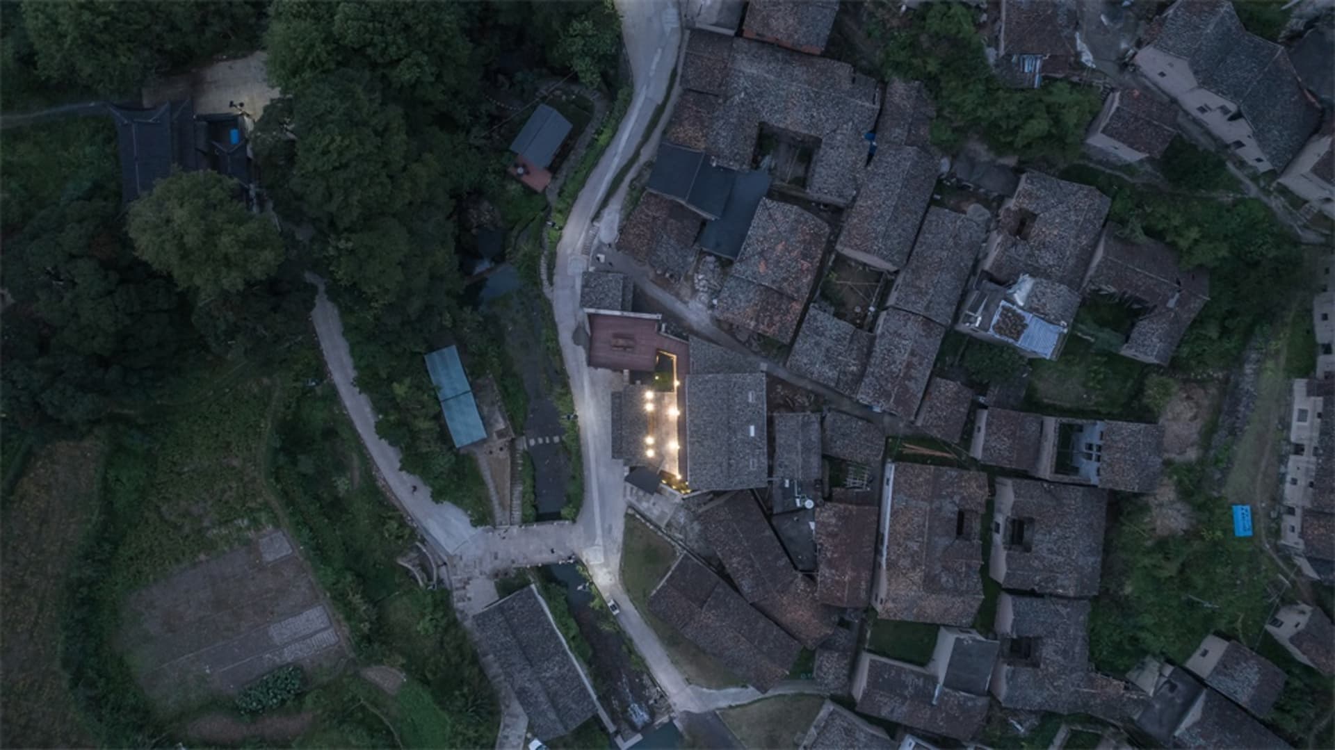 An aerial view of a village with stone-roofed houses surrounded by trees and fields.