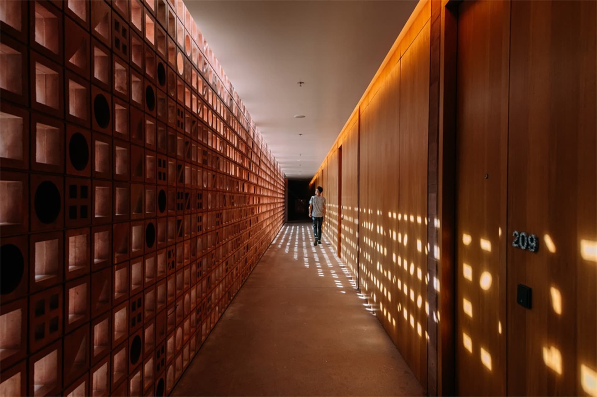 Hallway with minimalist design, illuminated with light fixtures, showing unique wall pattern with light and shadow effects.