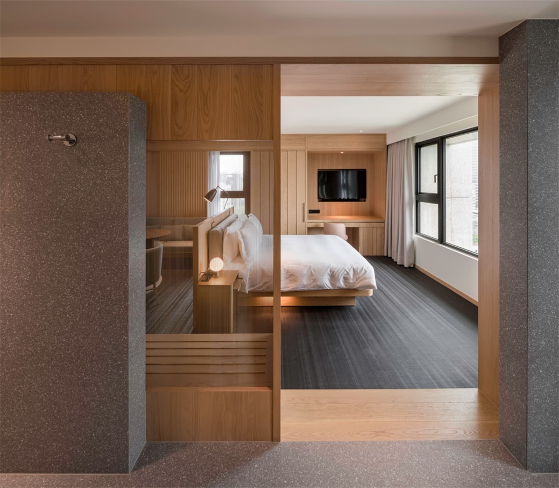 A modern bedroom suite featuring white furniture, wood-paneled walls, and carpeted flooring, with a large window and a view o