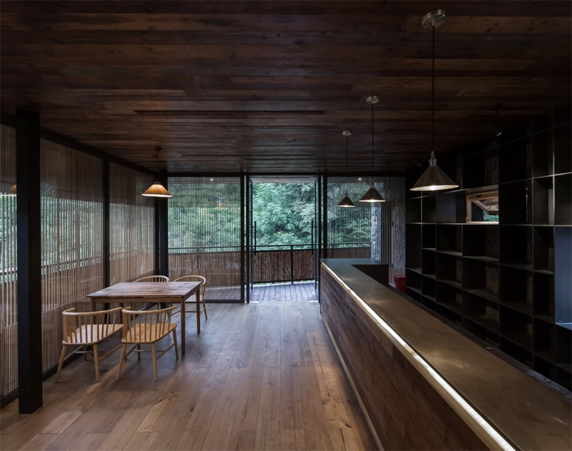 A modern restaurant with wooden interior and floor, featuring a long counter with lighting and a table with chairs in front o