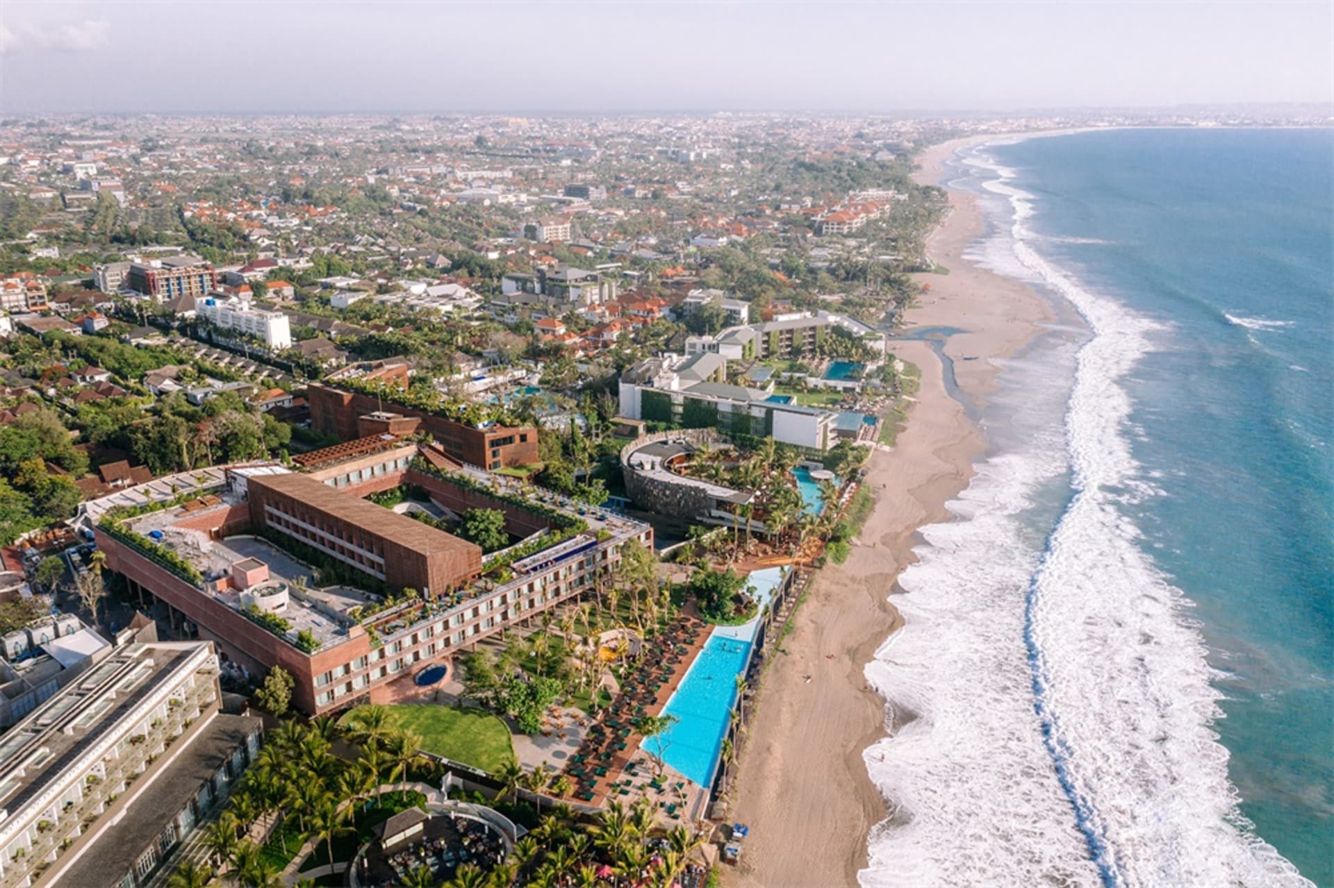 Aerial view of a beachside resort with a large pool area and multiple buildings.