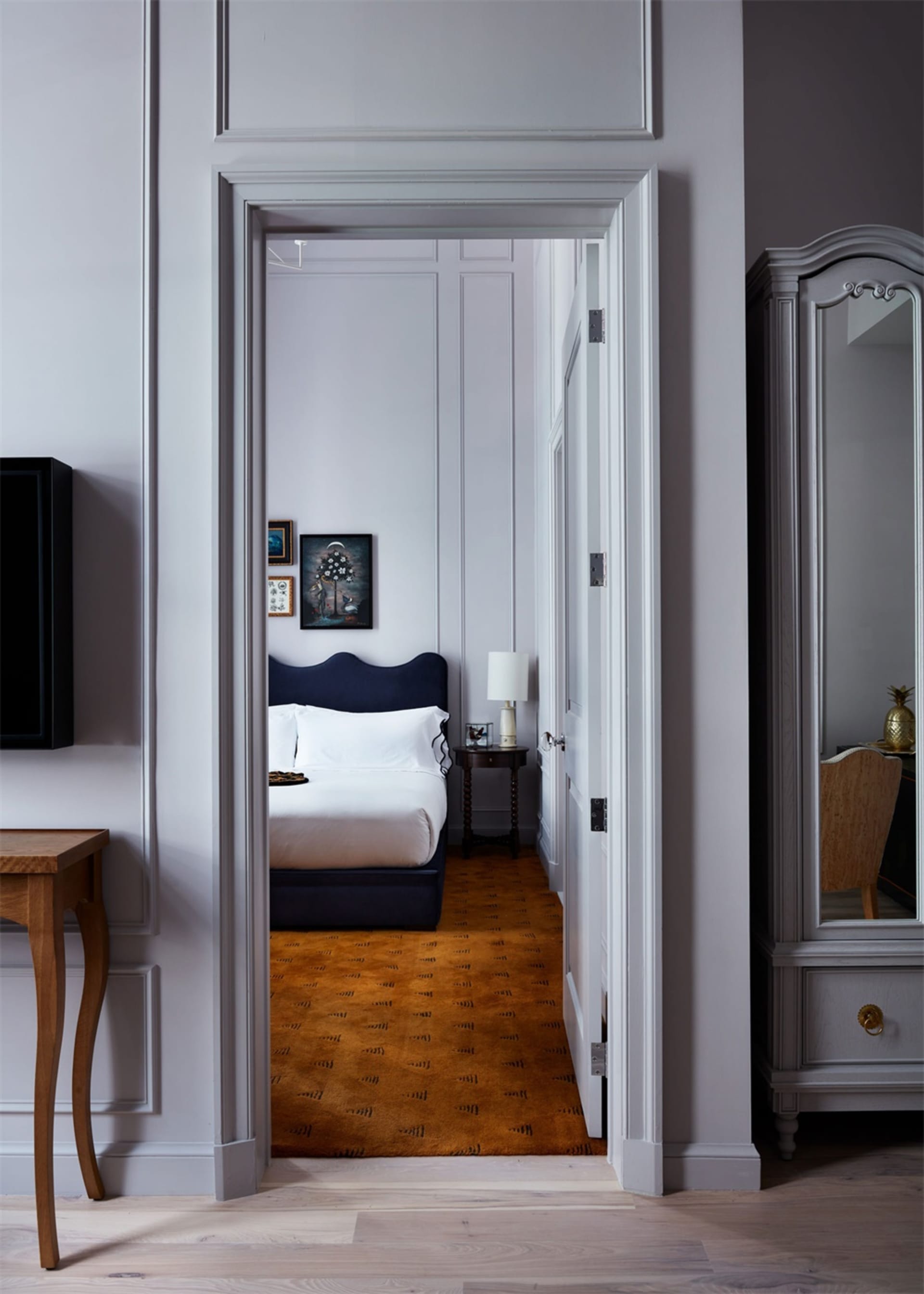 Modern bedroom with grey and white color palette, featuring a black upholstered bed, wooden floor, and framed art on the wall