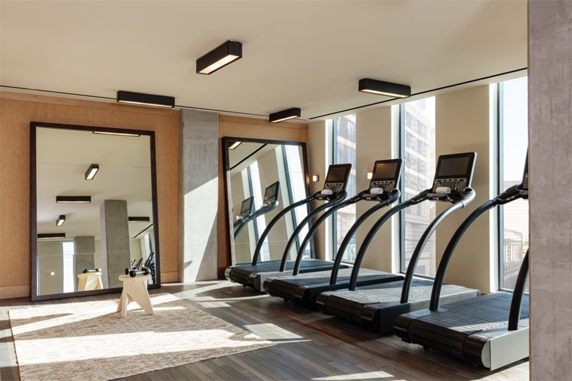 Modern gym with wooden floors, glass windows, and metal treadmills.