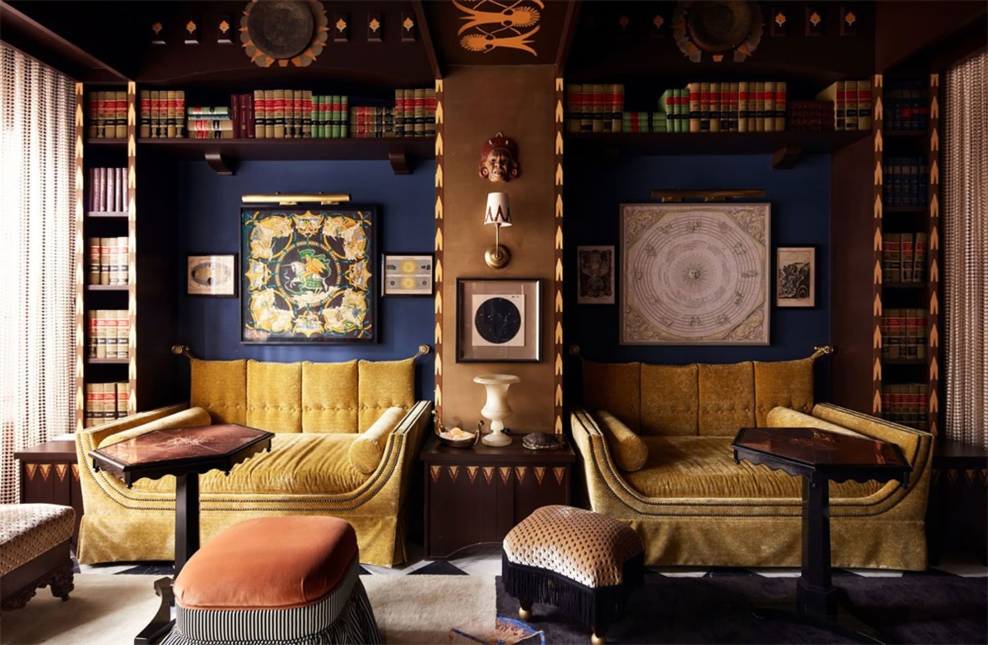 A modern living room with gold upholstery, dark wood accents, and silk artwork on navy walls.