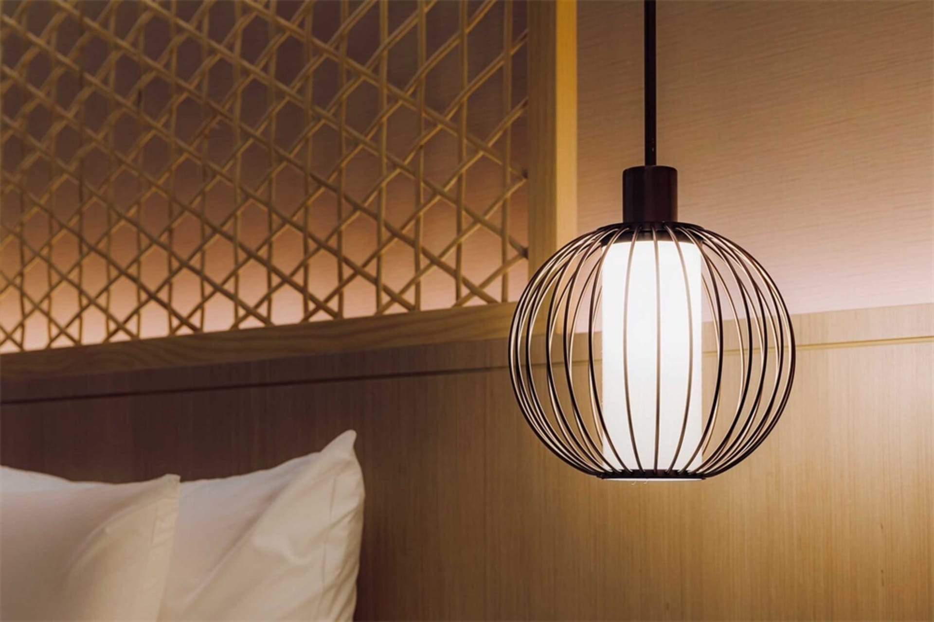 A minimalist bedroom with textured wood walls, white bedding, and a modern pendant light.