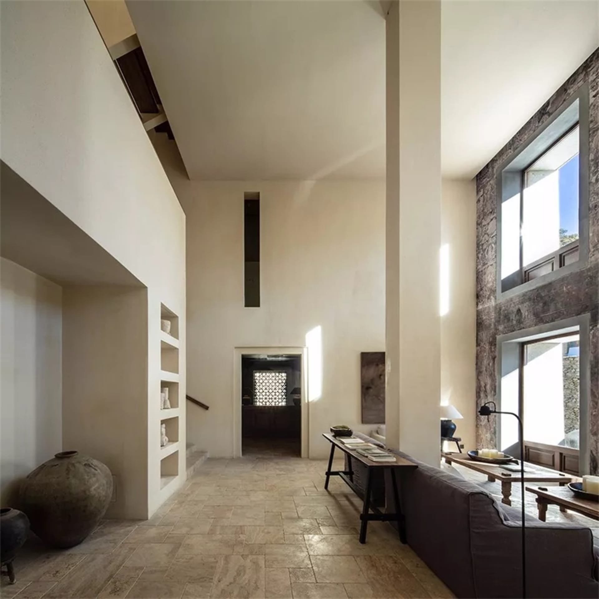 Modern minimalist living room with concrete flooring and walls, featuring a dark couch and a low table with books and decorat