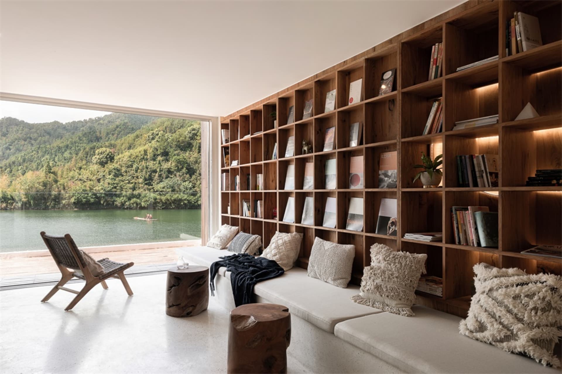 A minimalist living space featuring a large bookshelf filled with books and a cozy seating area by a waterfront.