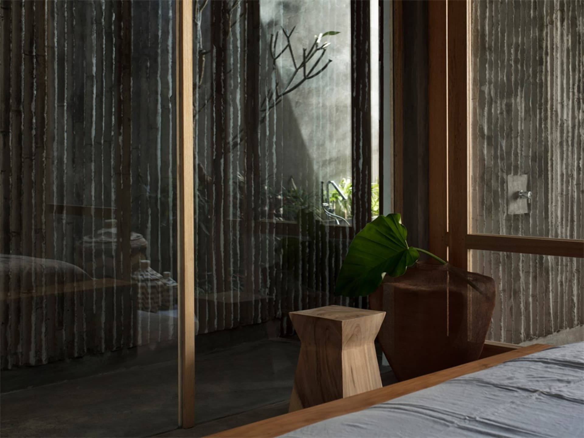 A minimalist interior space featuring a wooden stool and large green leaf plant.