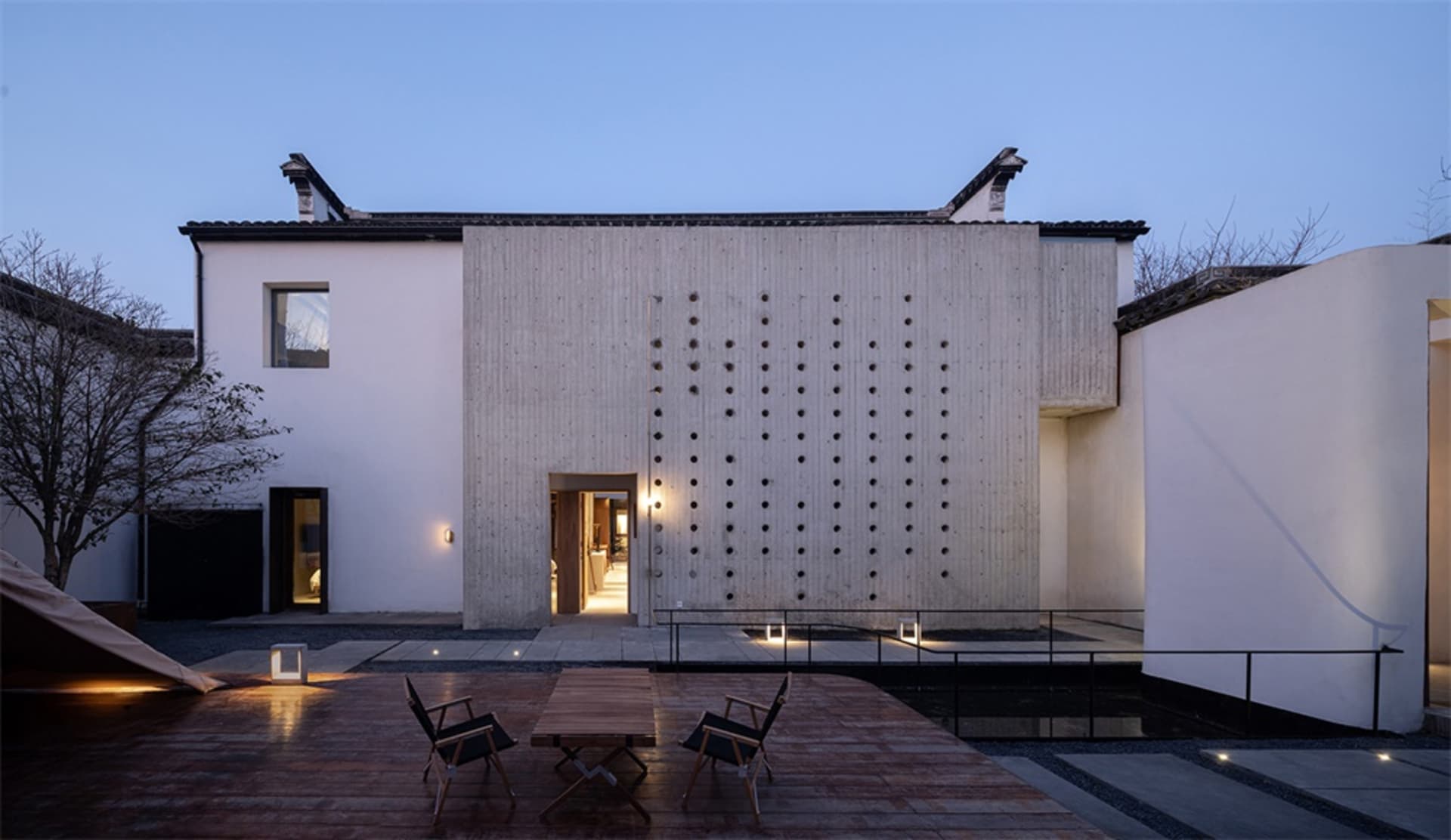 A minimalist residential exterior featuring a concrete structure with a grid of circular cutouts.