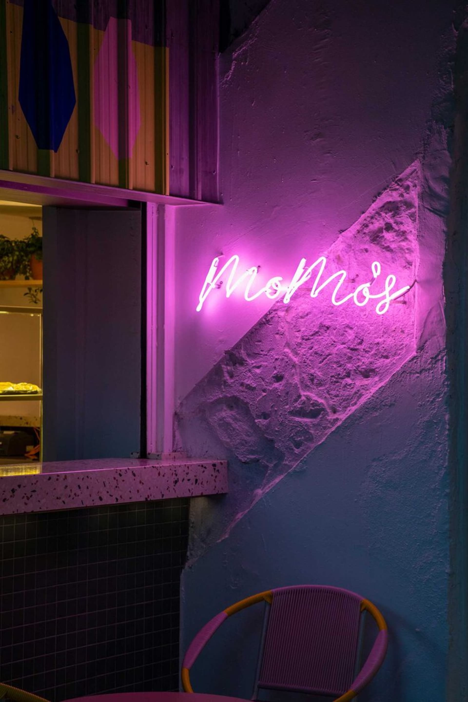 A modern bar area with pink neon lighting and a concrete wall.