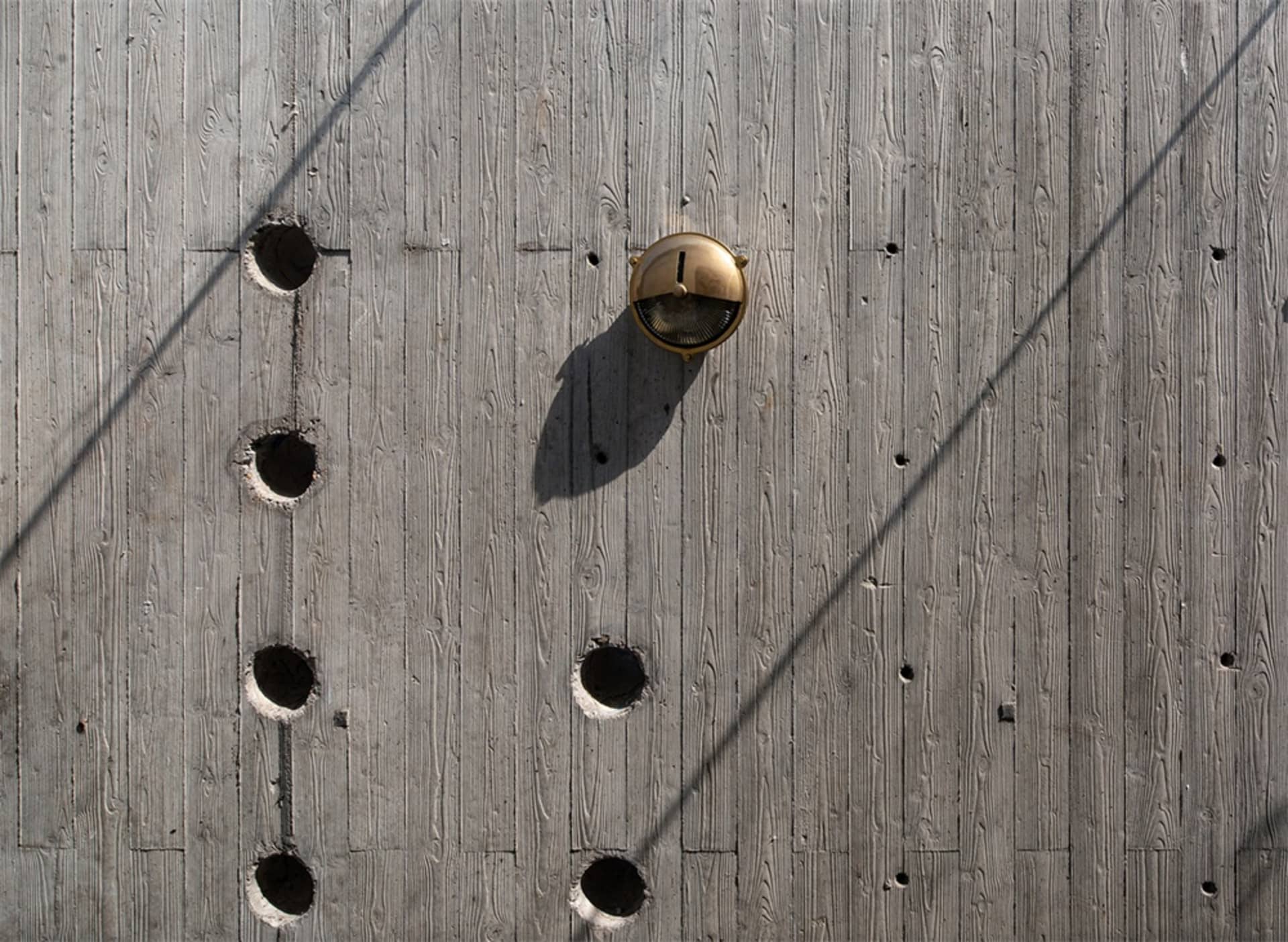 Concrete and wood cellar wall with circular cutouts and a brass light fixture.